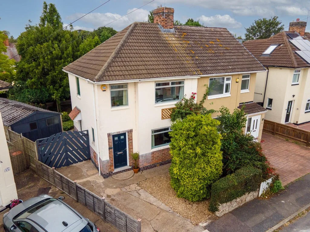 Merritt Estates. A two-story house with a brick chimney, white exterior walls, and a brown tiled roof with moss. The front yard has shrubs and a gravel path, and a blue front door.