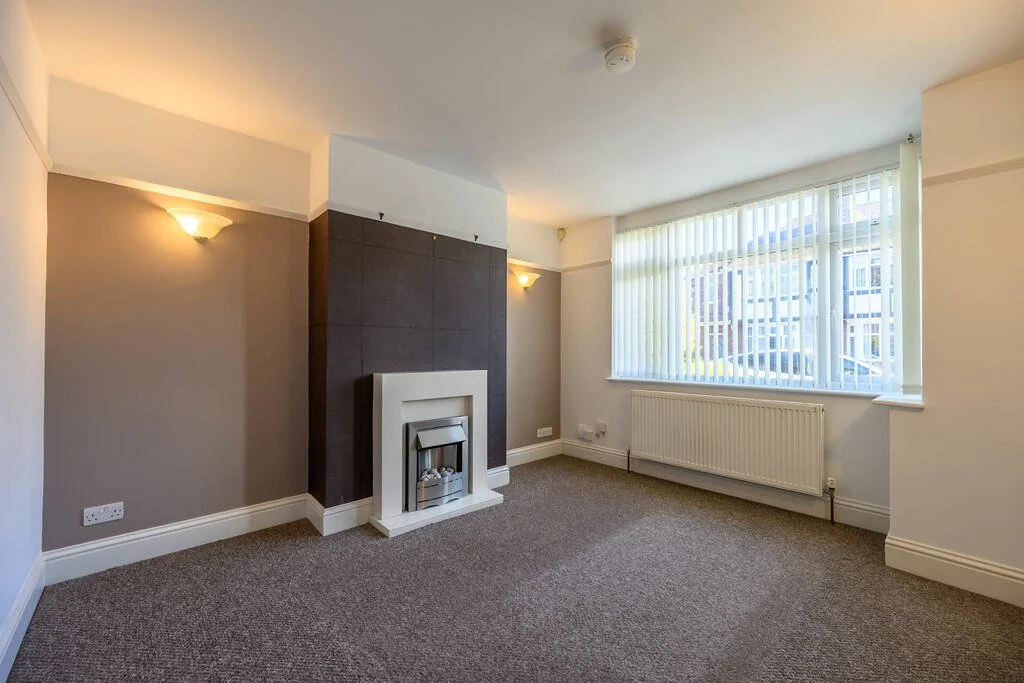Merritt Estates. Empty living room with beige and white walls, brown carpet, fireplace, large window with vertical blinds, radiator, and wall-mounted lights.