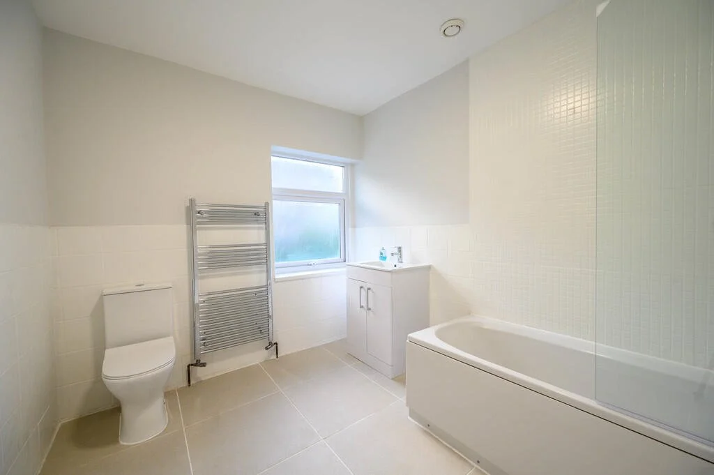 Merritt Estates. A bathroom with a white toilet, a heated towel rack, a small white vanity with a sink, a bathtub, and a frosted window.