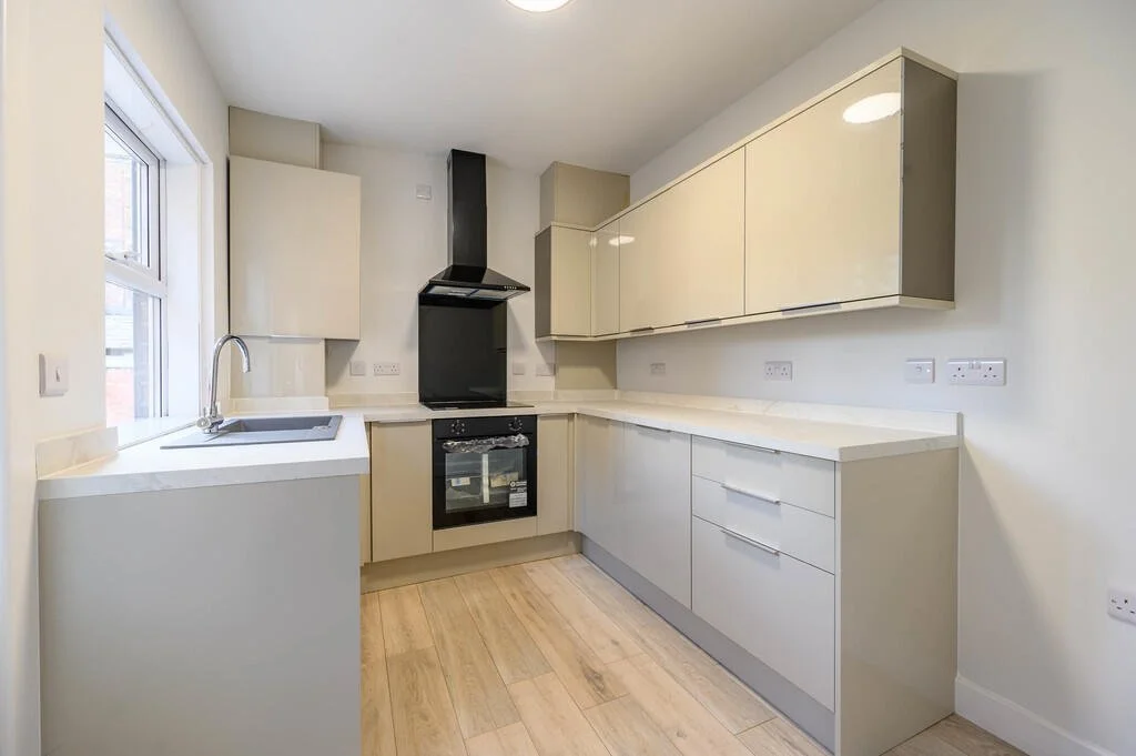 Merritt Estates. Modern kitchen with beige cabinets, white countertops, black oven, stove, extractor hood, and a window with a view outside.