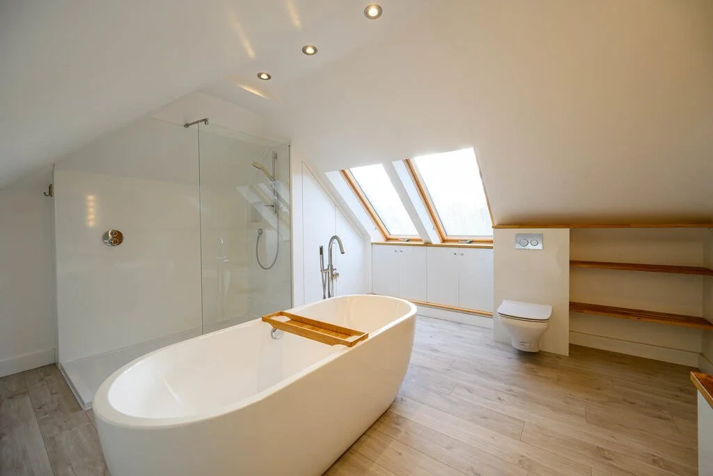 Merritt Estates. Bright attic bathroom with a freestanding bathtub, skylight windows, a walk-in shower, and built-in shelves.
