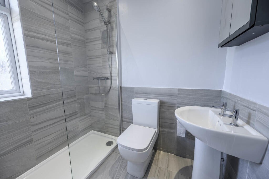 Merritt Estates. Small modern bathroom with a shower, toilet, and pedestal sink, grey tiles, and a window.