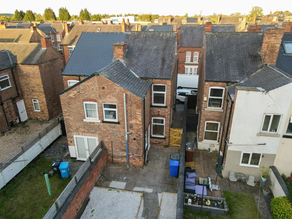 Merritt Estates. Aerial view of a row of tightly packed brick and stucco houses with small backyard patios, trash bins, garden furniture, and fences in a suburban neighbourhood.