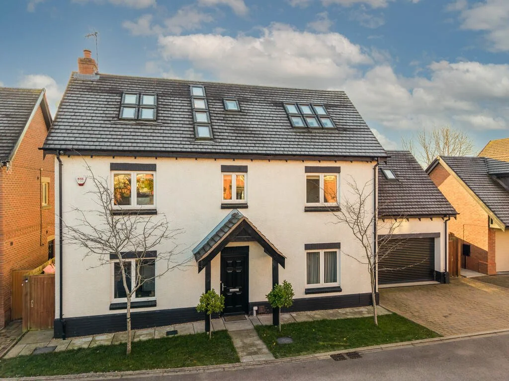 A two-story white house with black trim and roof, featuring skylights on the roof and a small porch over the front door. There are two leafless trees in front and a sidewalk and grass yard.