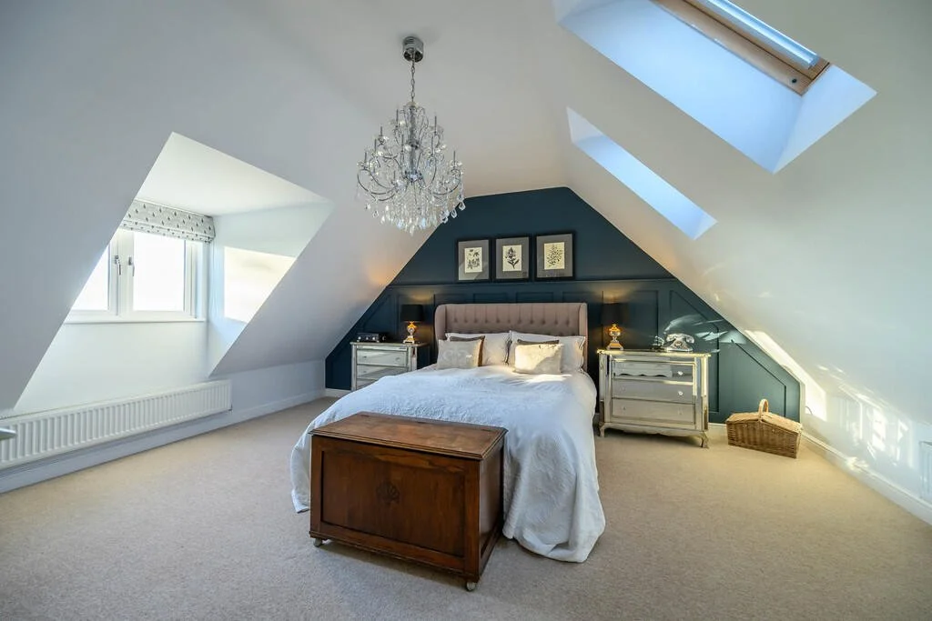 Bedroom with sloped ceiling, skylights, chandelier, and a bed with a tufted headboard.