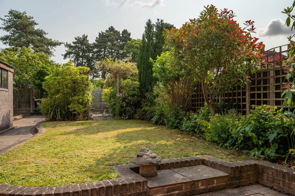 Merritt Estates. A backyard garden with a lawn, various shrubs and trees, a small stone garden ornament, and a wooden fence along the back and right sides.