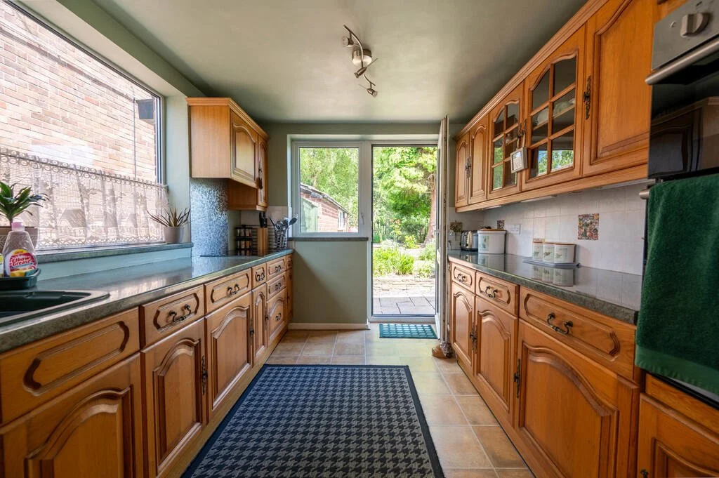A kitchen with wooden cabinets, a window ledge with potted plants, and a view outside to a garden and trees.