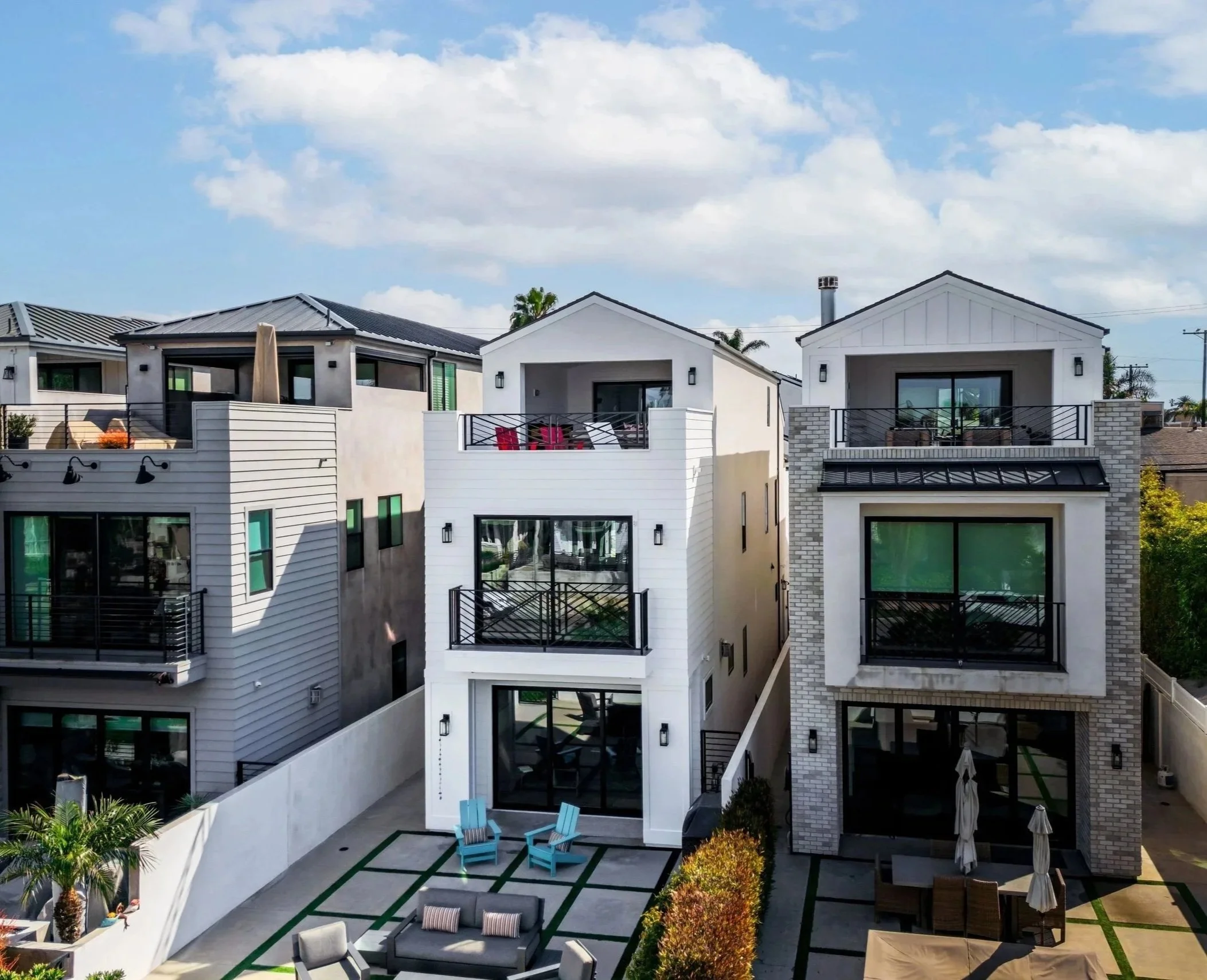 Modern residential buildings with rooftop terraces and outdoor seating areas under a partly cloudy sky in Huntington Beach.