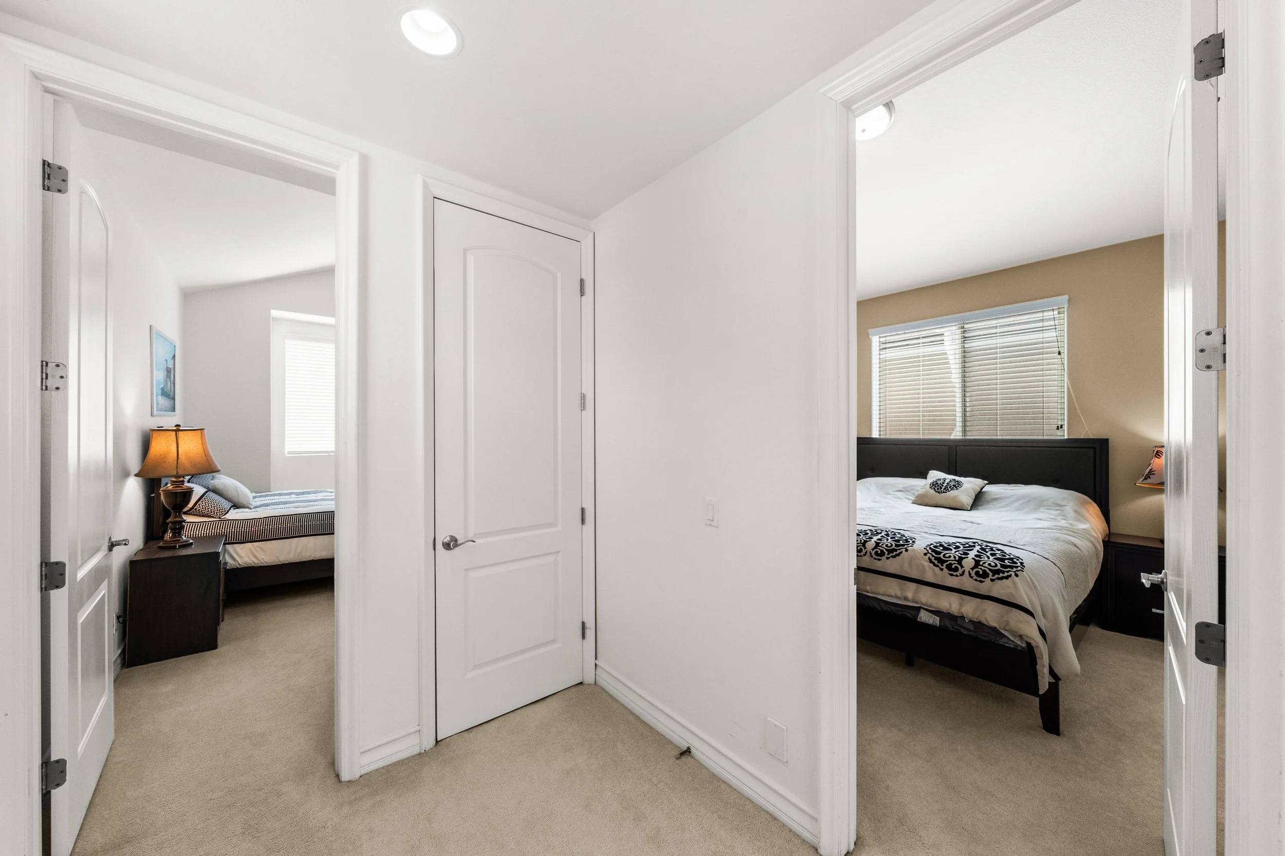 Interior view of a hallway leading to two bedrooms with open doors, showing beds with bedding and windows with blinds.
