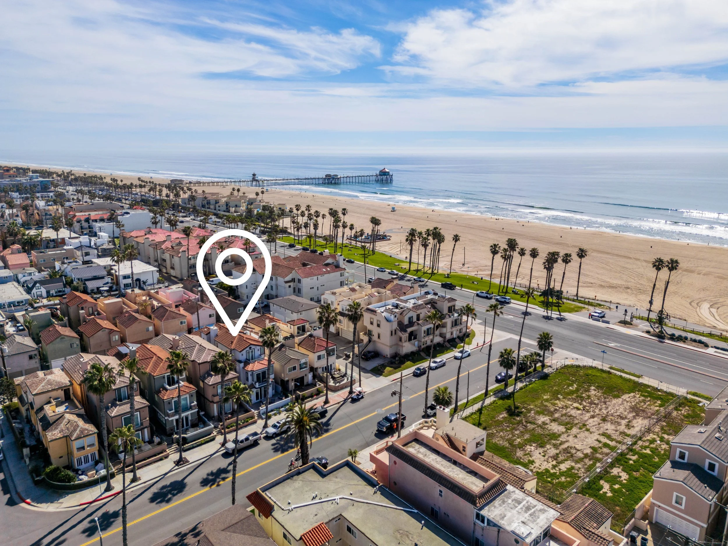Aerial view of a beach with a pier extending into the ocean, surrounded by a neighborhood with houses and palm trees along the coast.