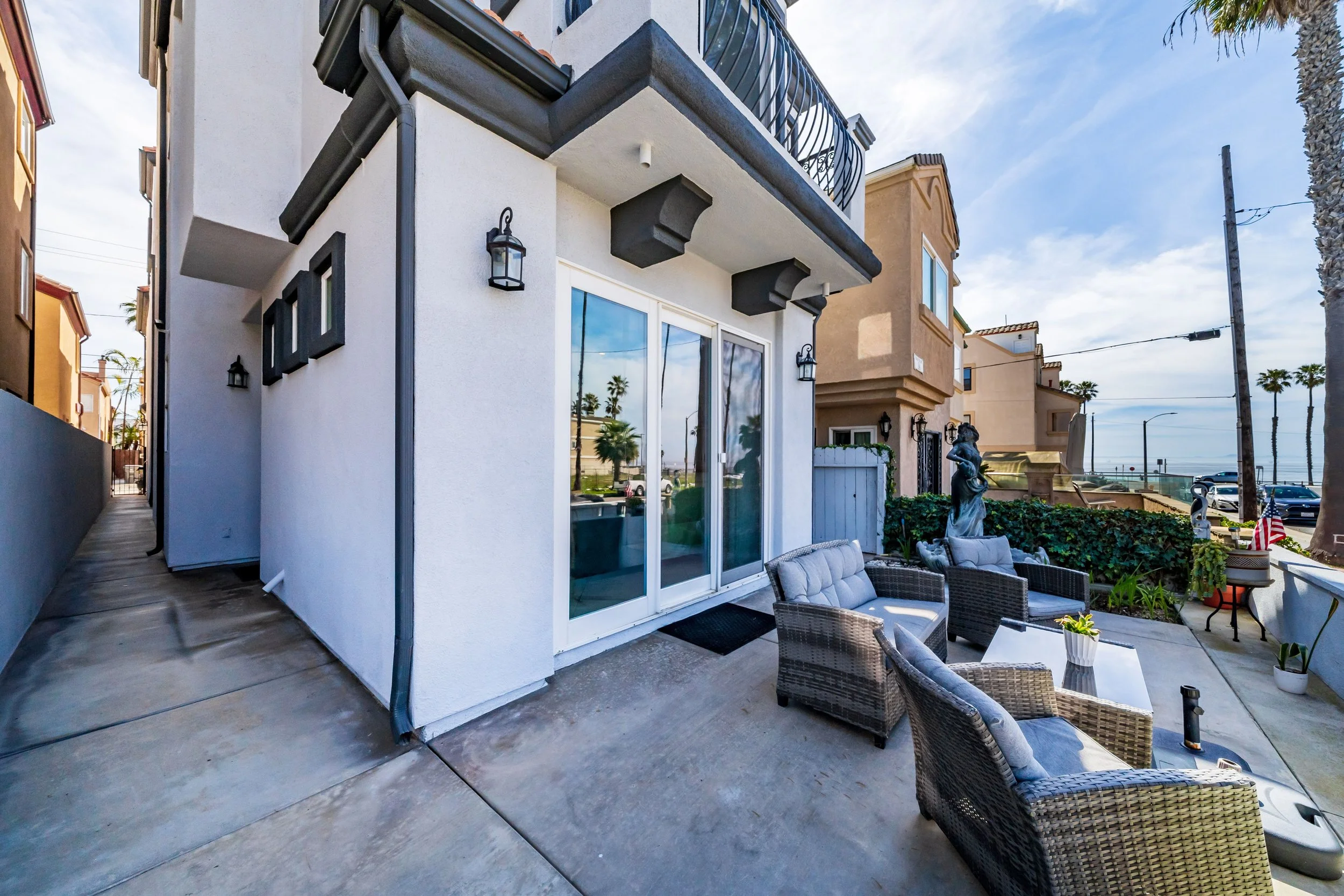 Outdoor patio area with wicker chairs, potted plants, and a view of neighboring buildings and palm trees.