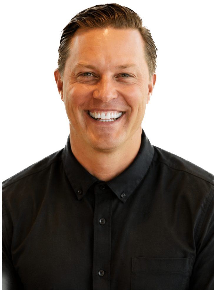 Nik Hennessee, a man with light skin and brown hair, smiling broadly with white teeth, wearing a black button-up shirt.
