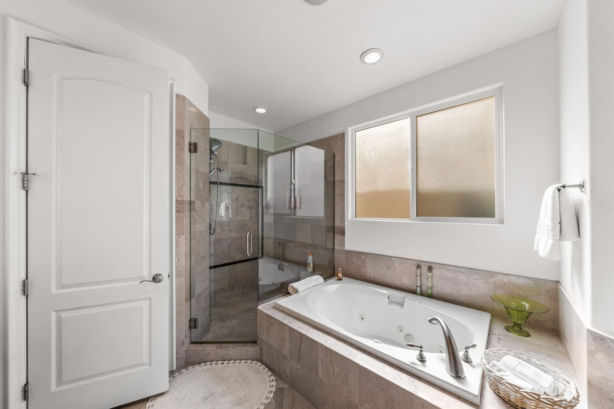 Modern bathroom with walk-in shower, bathtub, and large frosted windows, all in neutral tones.