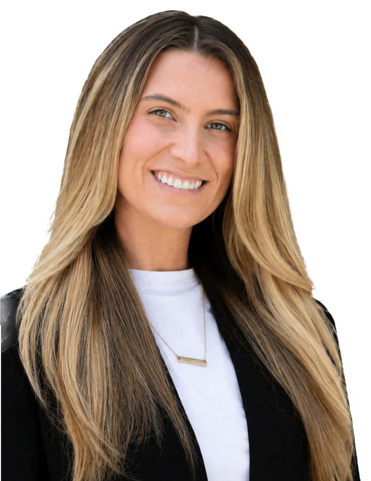 A young woman with long, wavy blonde hair smiling at the camera, wearing a black blazer, white shirt, and a gold necklace, with a blurred colorful background.