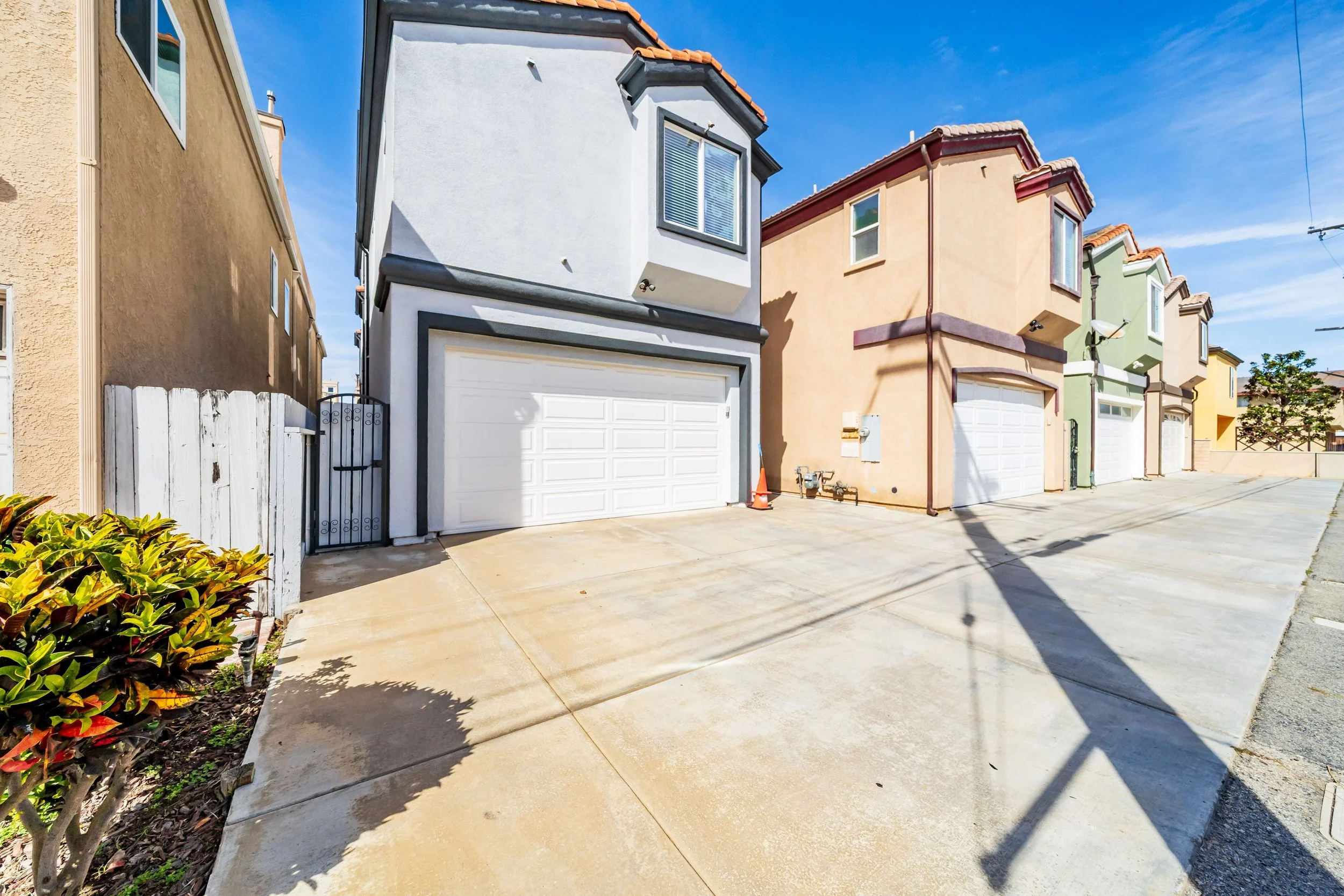 Colorful row of townhouses with driveway in the foreground, blue sky, and sunny weather.