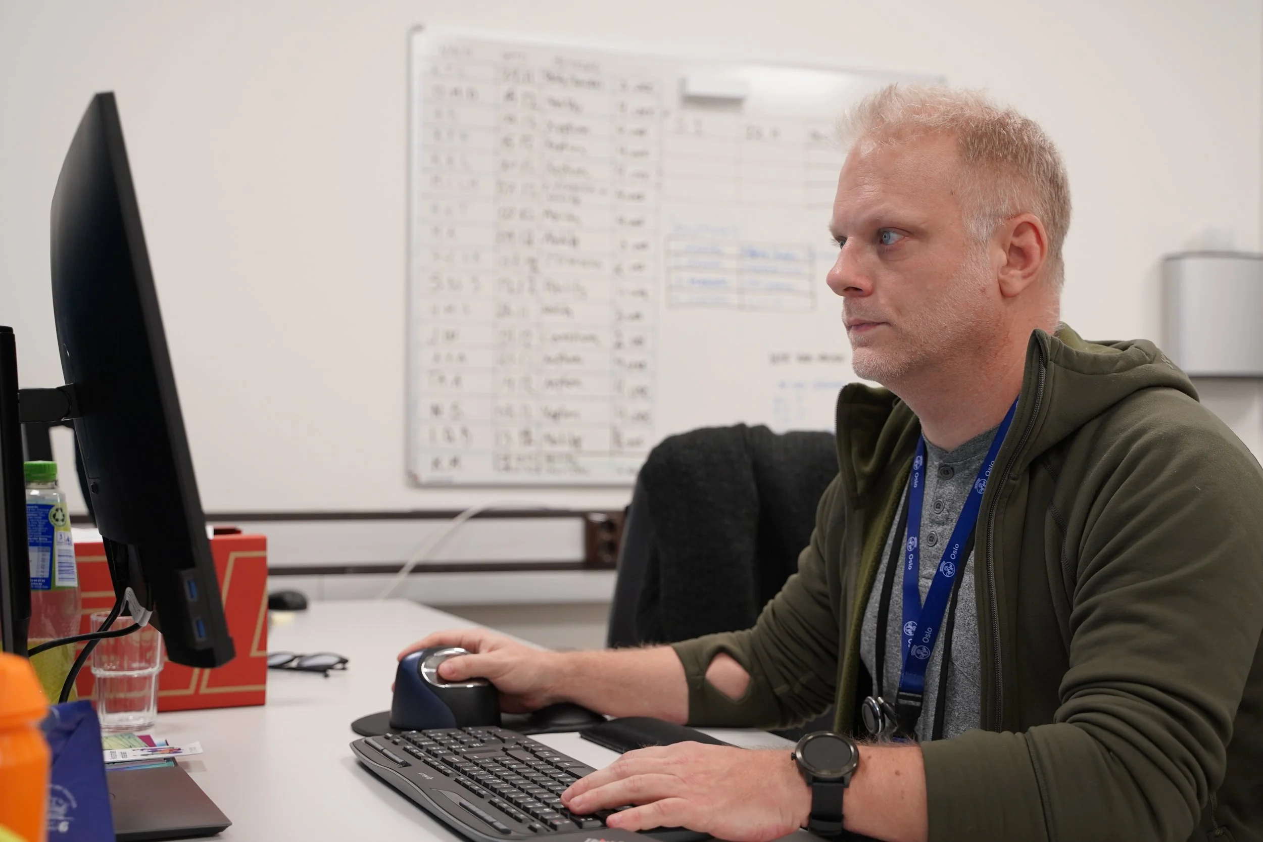 Karl sitter og konsentrerer seg foran en PC, i bakgrunnen er en whiteboard med ting skrevet opp på.