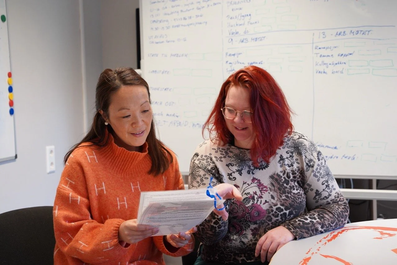 To kvinner på Fontenehuset sitter ved et bord og går gjennom dokumenter om studiestøtte, med en tavle med notater i bakgrunnen.