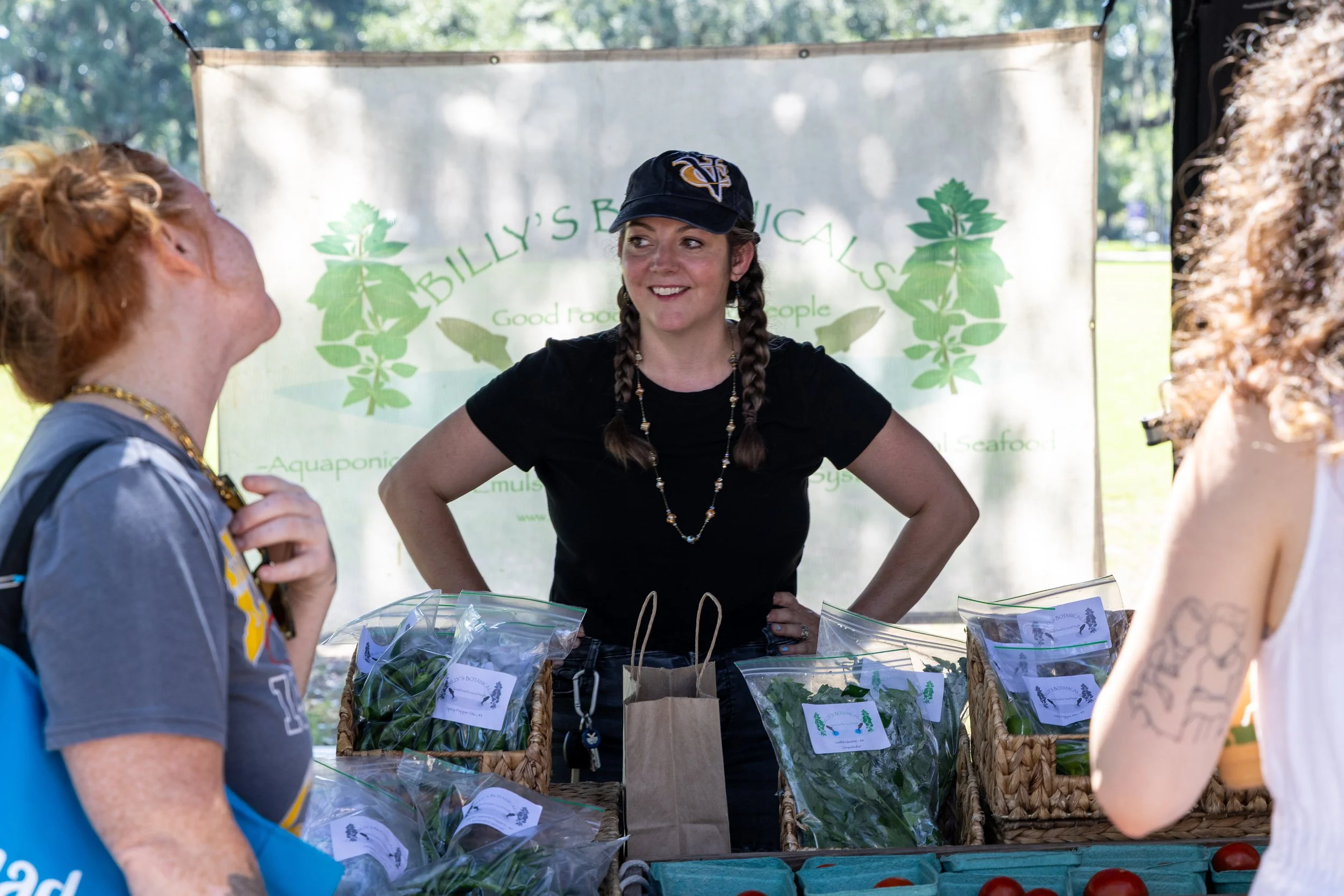 A staff member from Billy’s Botanicals chats with customers at the Forsyth Farmers’ Market Saturday Market. In front of them, a table overflows with bags of fresh herbs and leafy greens grown on their Coastal Georgia farm. Photo by Brian Bonsteel.