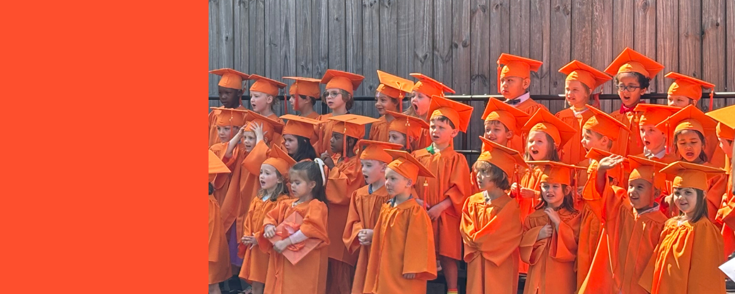 Group of children wearing orange graduation gowns and caps, celebrating during a graduation ceremony outdoors.