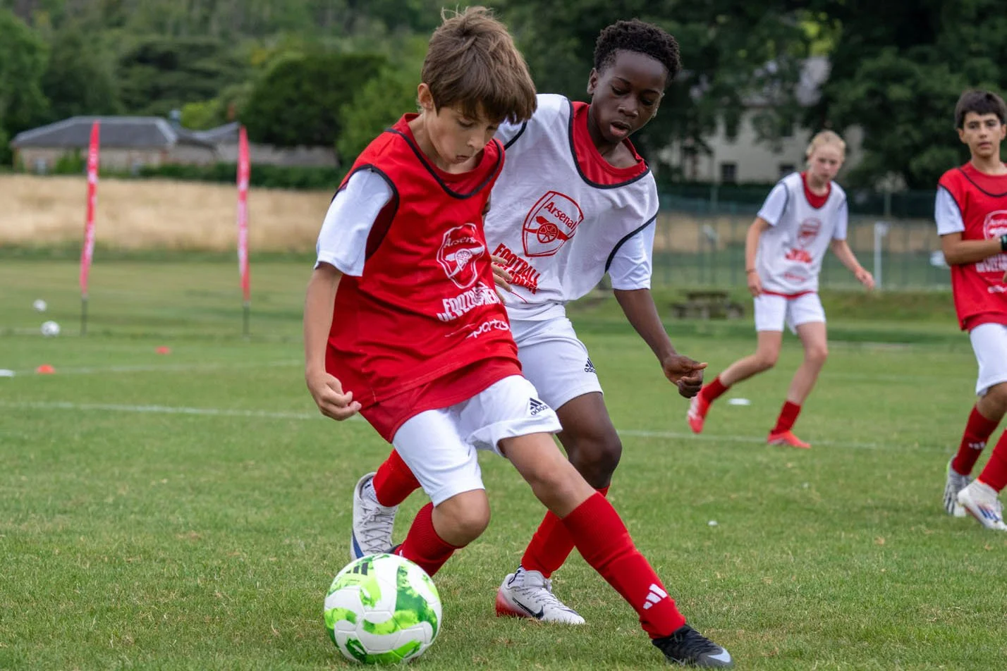 young boys playing soccer on a grassy field, competing for the ball, with trees and hills in the background.