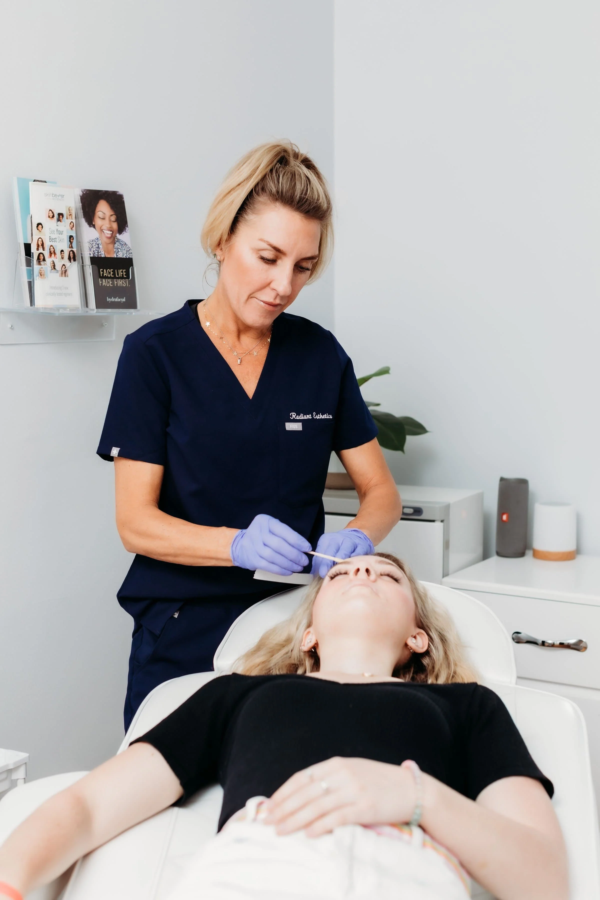 A woman lying on a chair receiving a skincare treatment from a esthetician in a clinic.