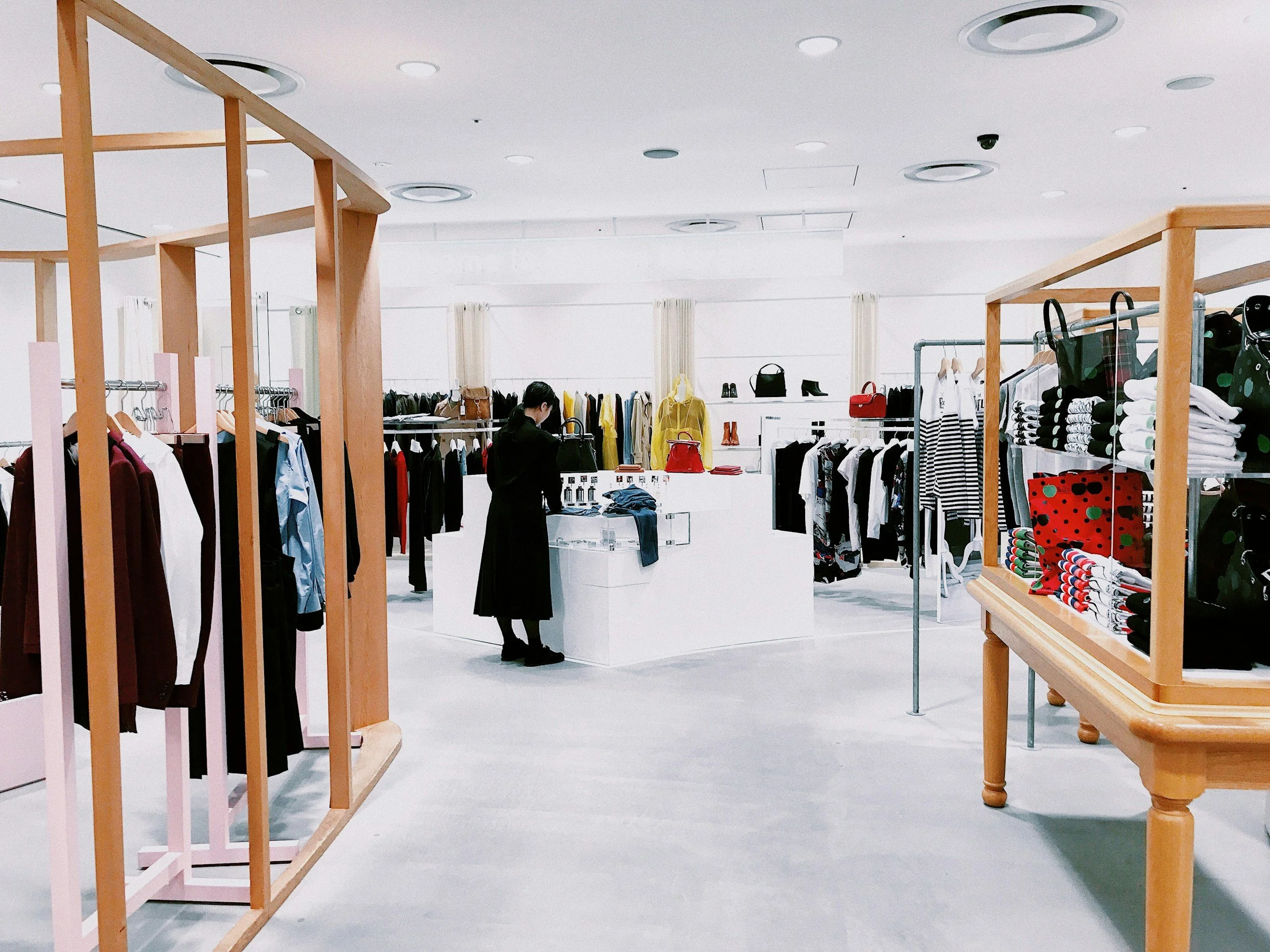 Interior of a clothing store with racks of clothes, handbags, and accessories. A person is shopping in the middle of the store.