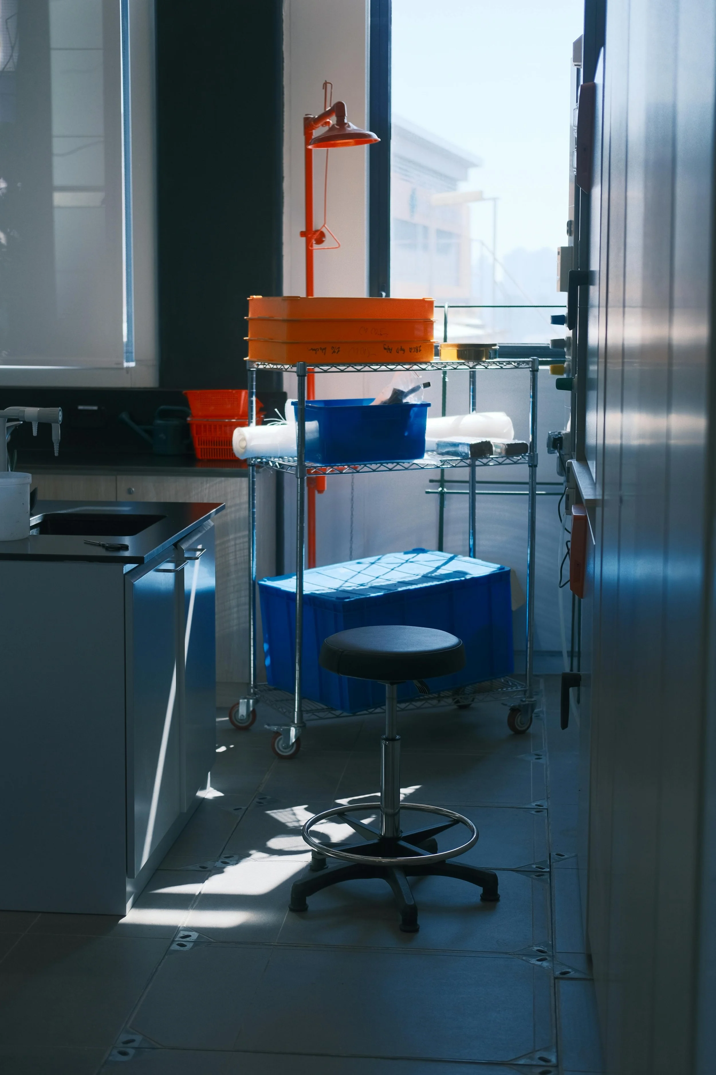 Medical or laboratory storage room with shelves, containers, and a stool near a window allowing natural light.