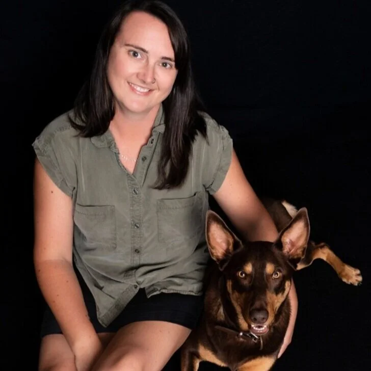 Woman sitting with a brown dog against a black background.
