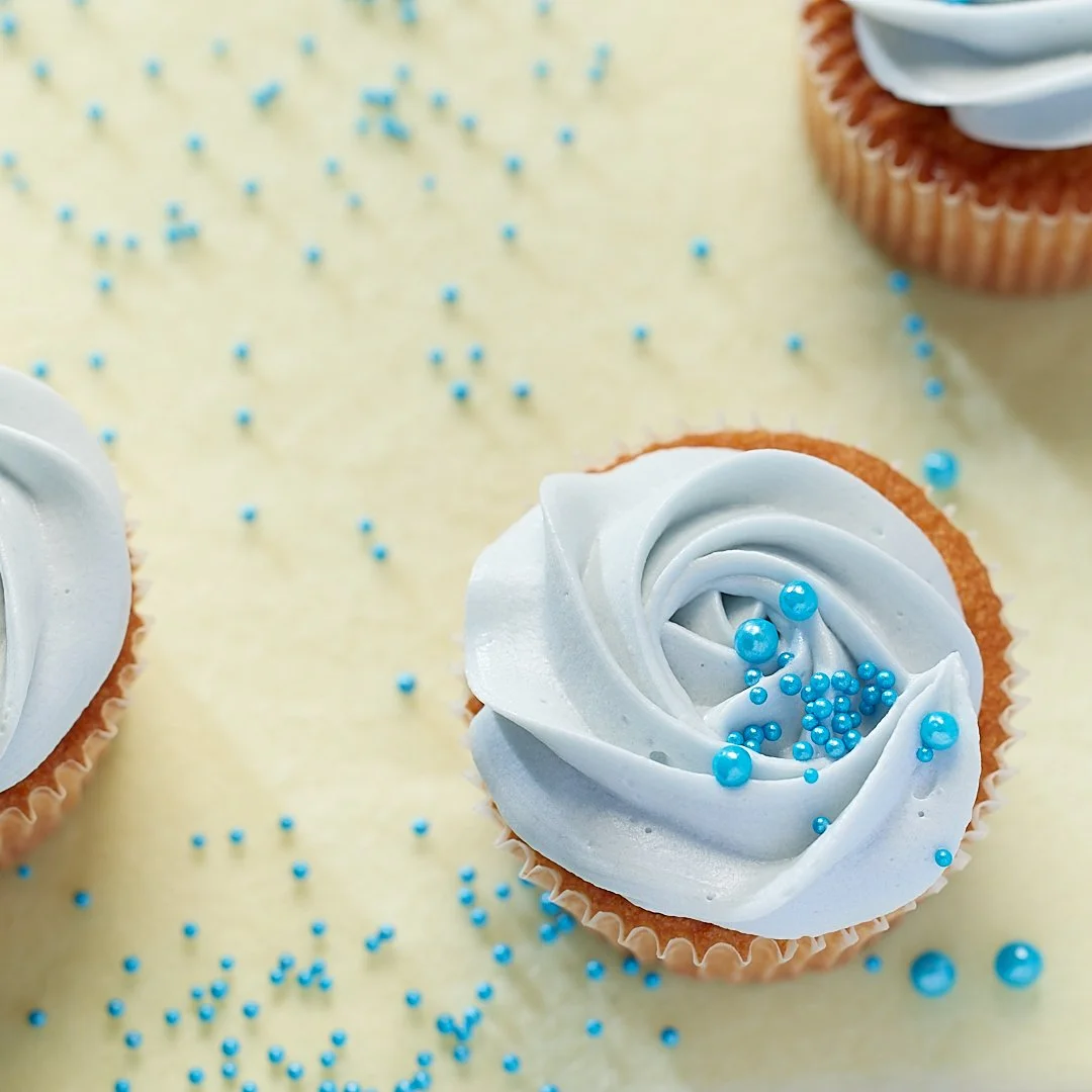 Cupcakes with light blue frosting and blue sprinkles on a light background.
