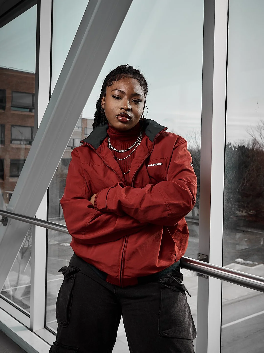 Person in a red jacket leaning against a railing in a modern building corridor, with large windows in the background.