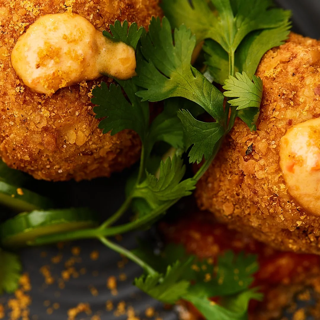 Close-up of crispy fried croquettes topped with a creamy sauce, garnished with fresh cilantro and sliced jalapeños.