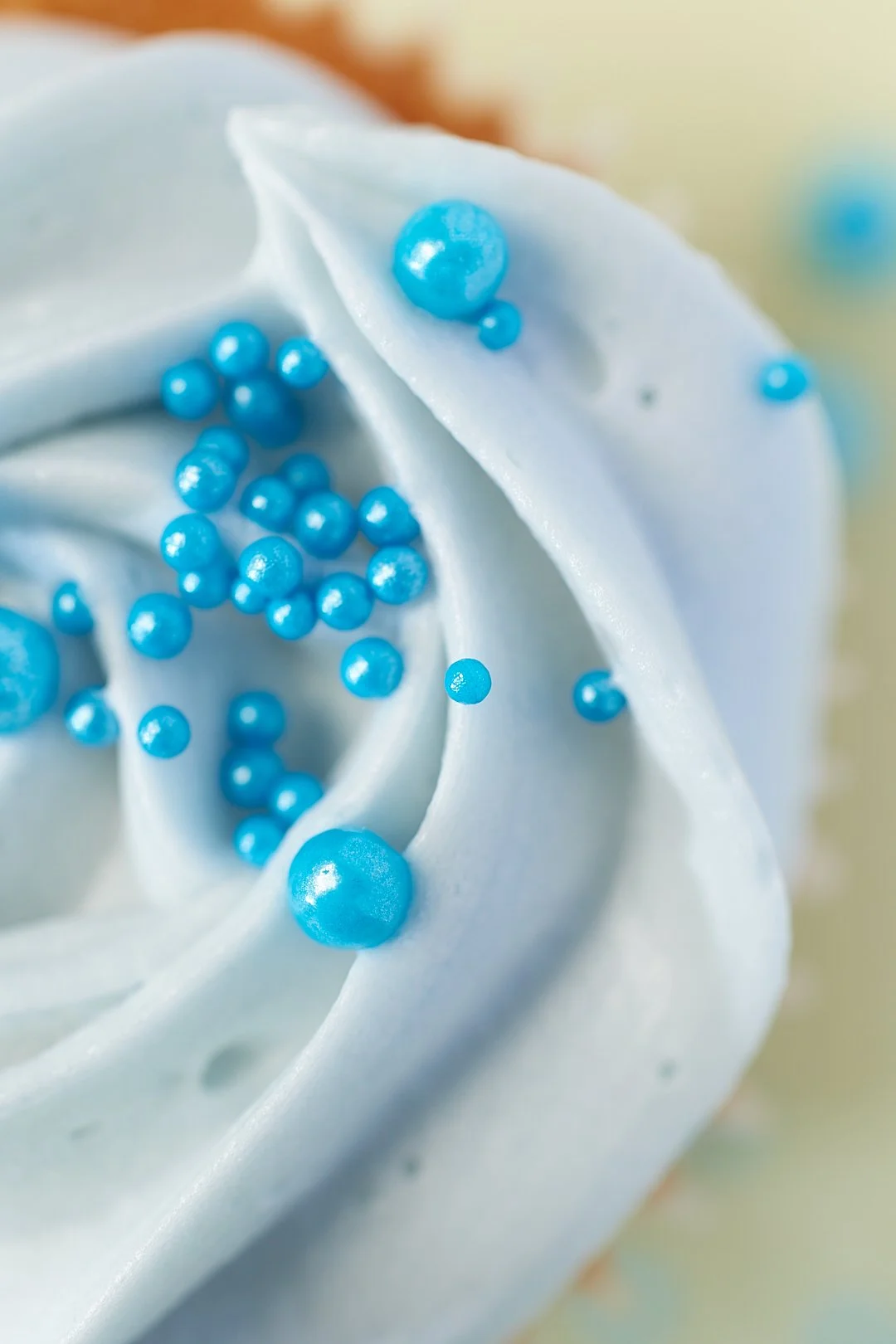 Close-up of a cupcake with light blue frosting and blue sugar pearls.