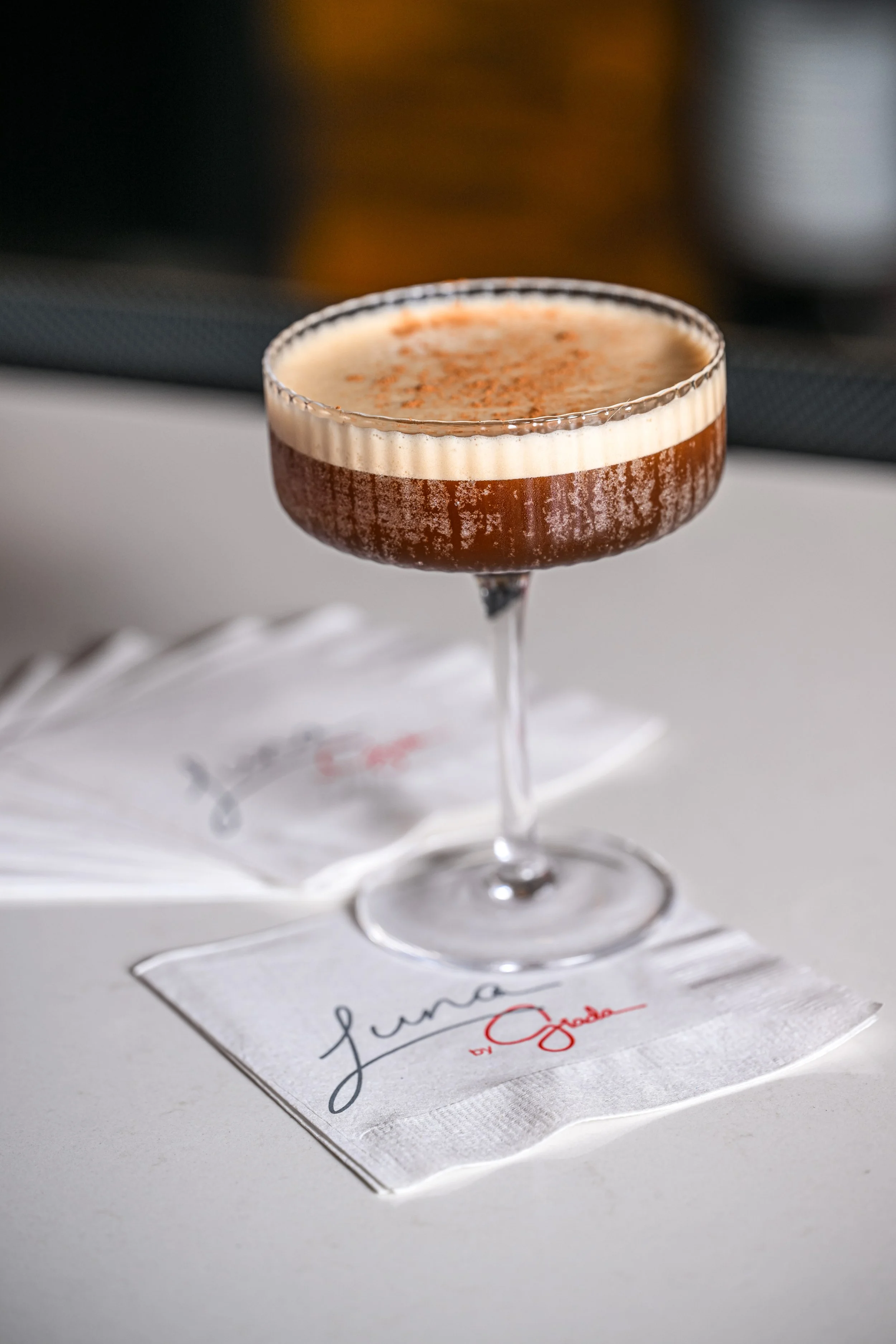 A cocktail in a coupe glass with a snowy white foam topping sprinkled with spices, placed on a gratitude card on a white surface.