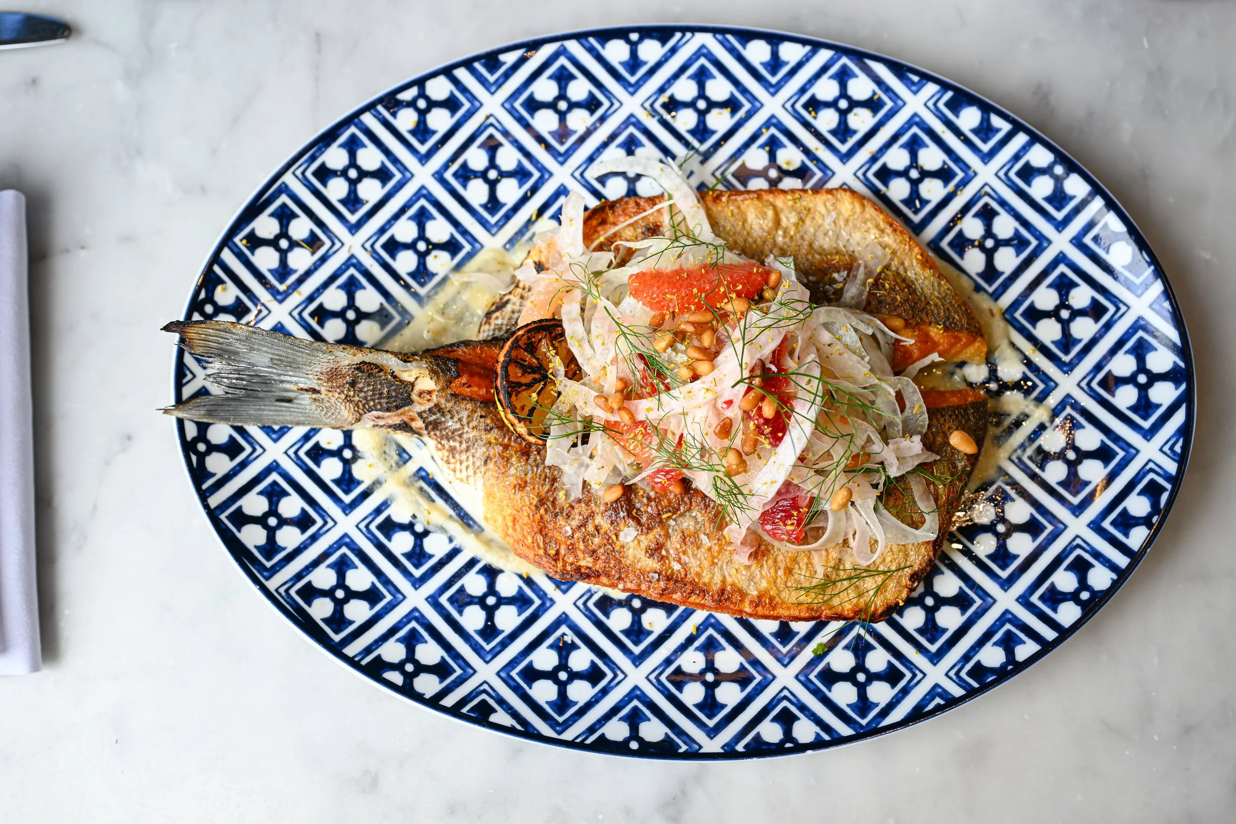 A whole cooked fish topped with a fresh salad on a blue and white patterned plate.