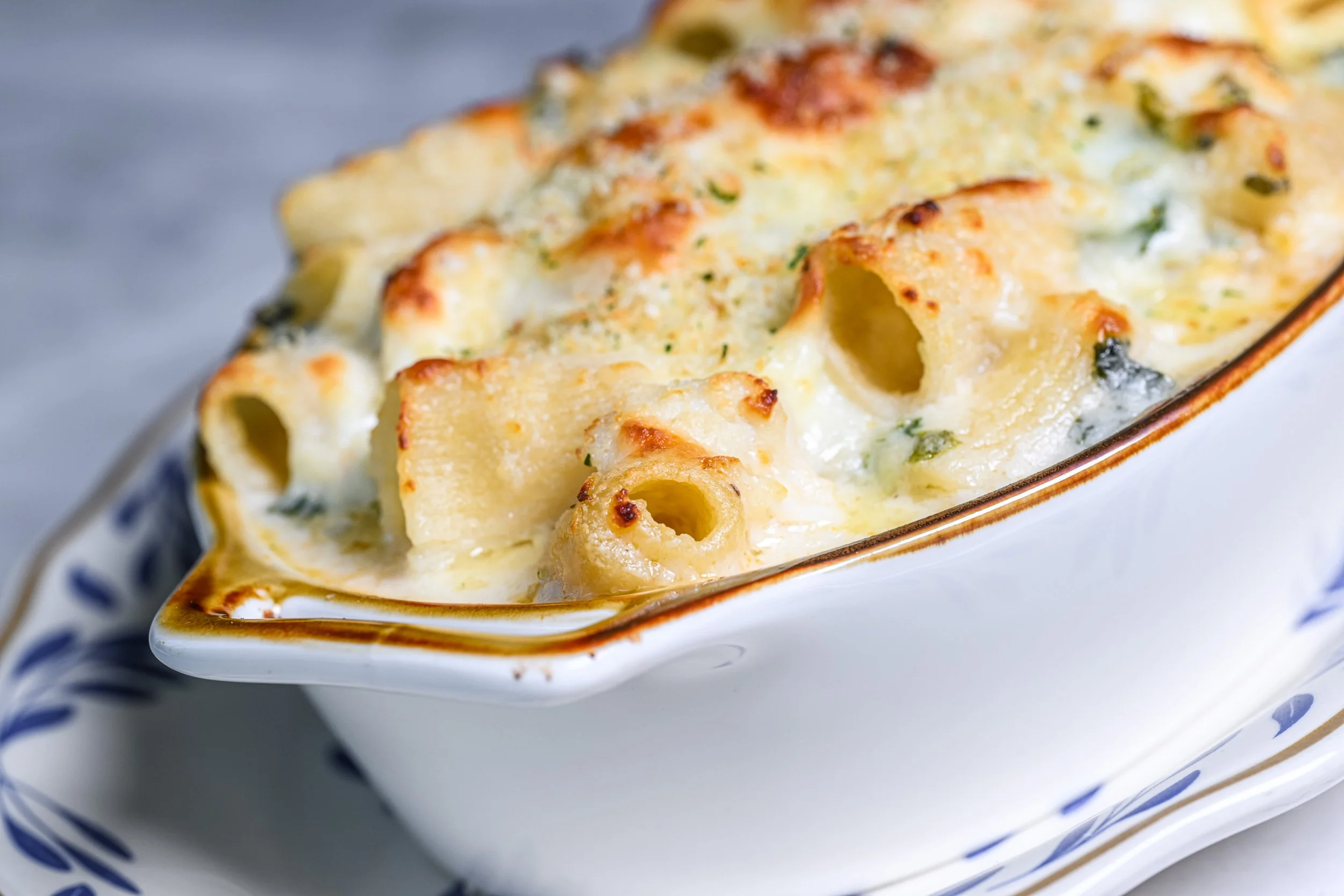 Baked pasta casserole with cheese and herbs in a white dish with blue trim.