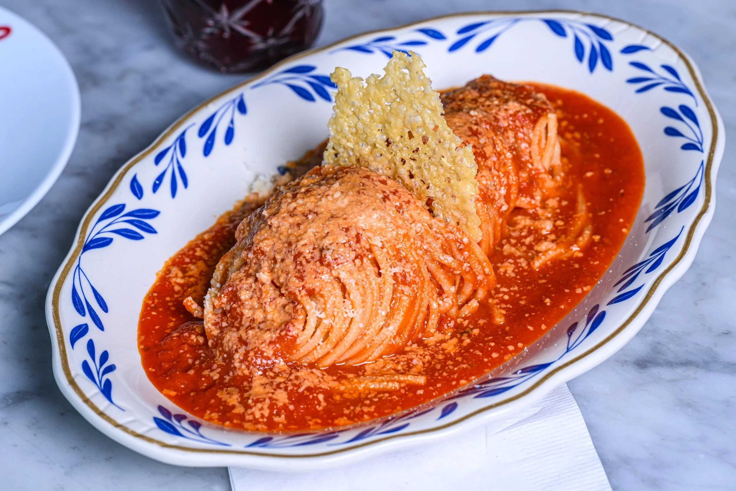 Plate of spaghetti with red sauce, topped with grated cheese, served with a crispy Parmesan cheese crisp