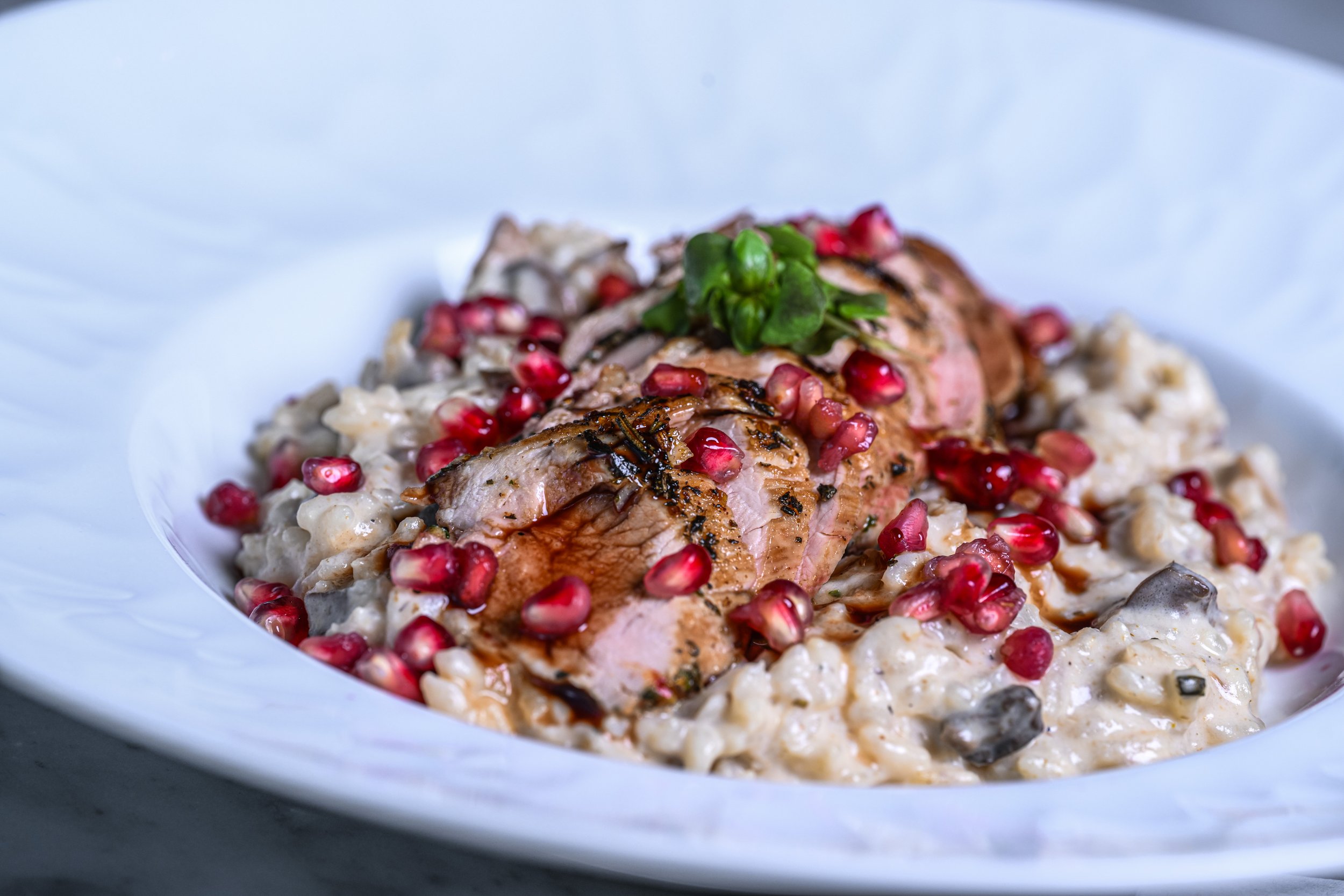 A plate of creamy risotto topped with grilled salmon, garnished with pomegranate seeds and a sprig of herbs.