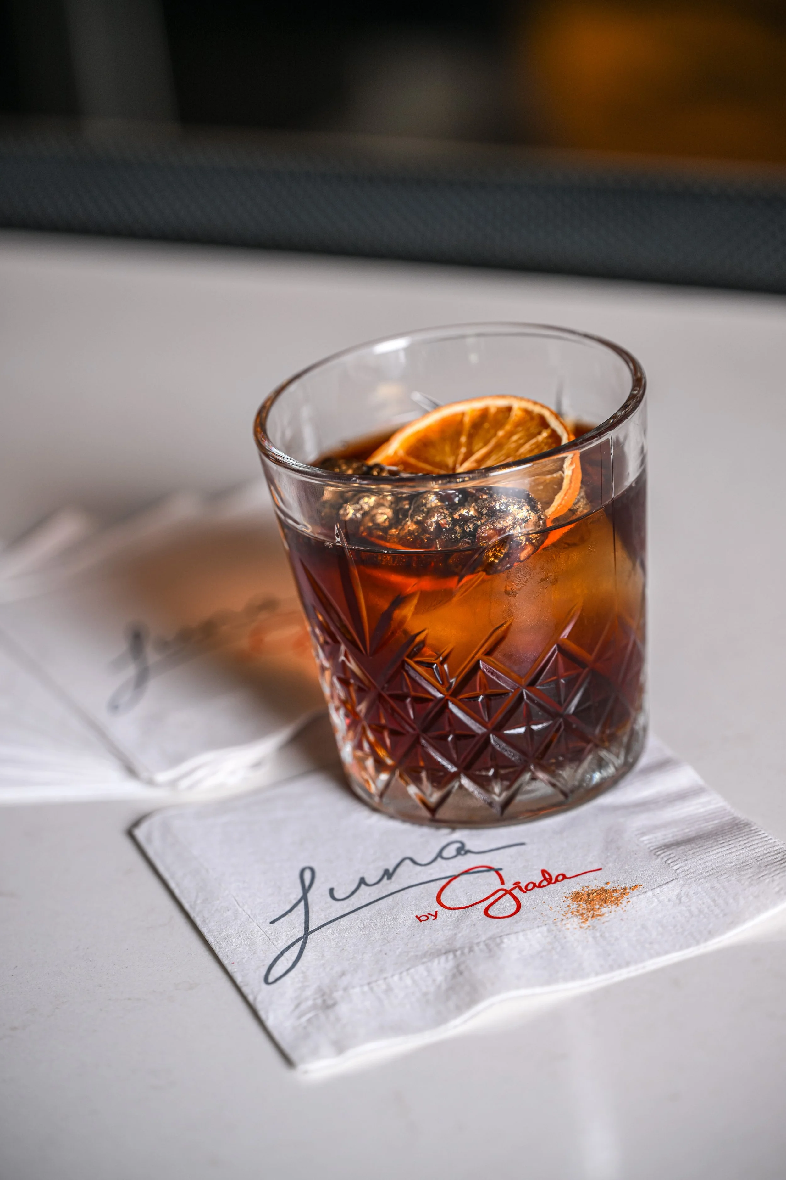 A glass of iced tea garnished with a dried orange slice, placed on a napkin with the words 'Luna by Giada.'
