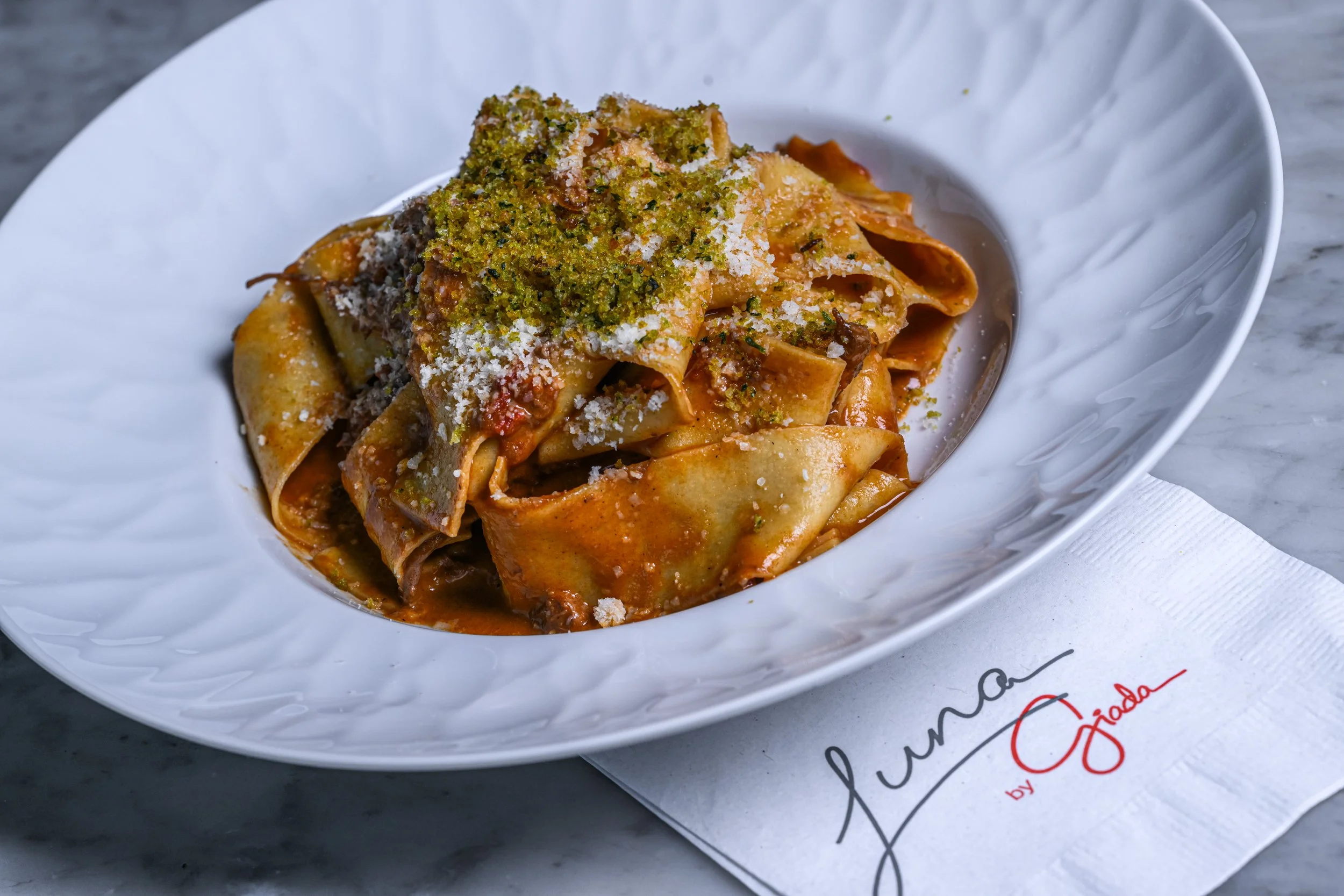 Plate of lasagna topped with chopped herbs and grated cheese on a white plate.