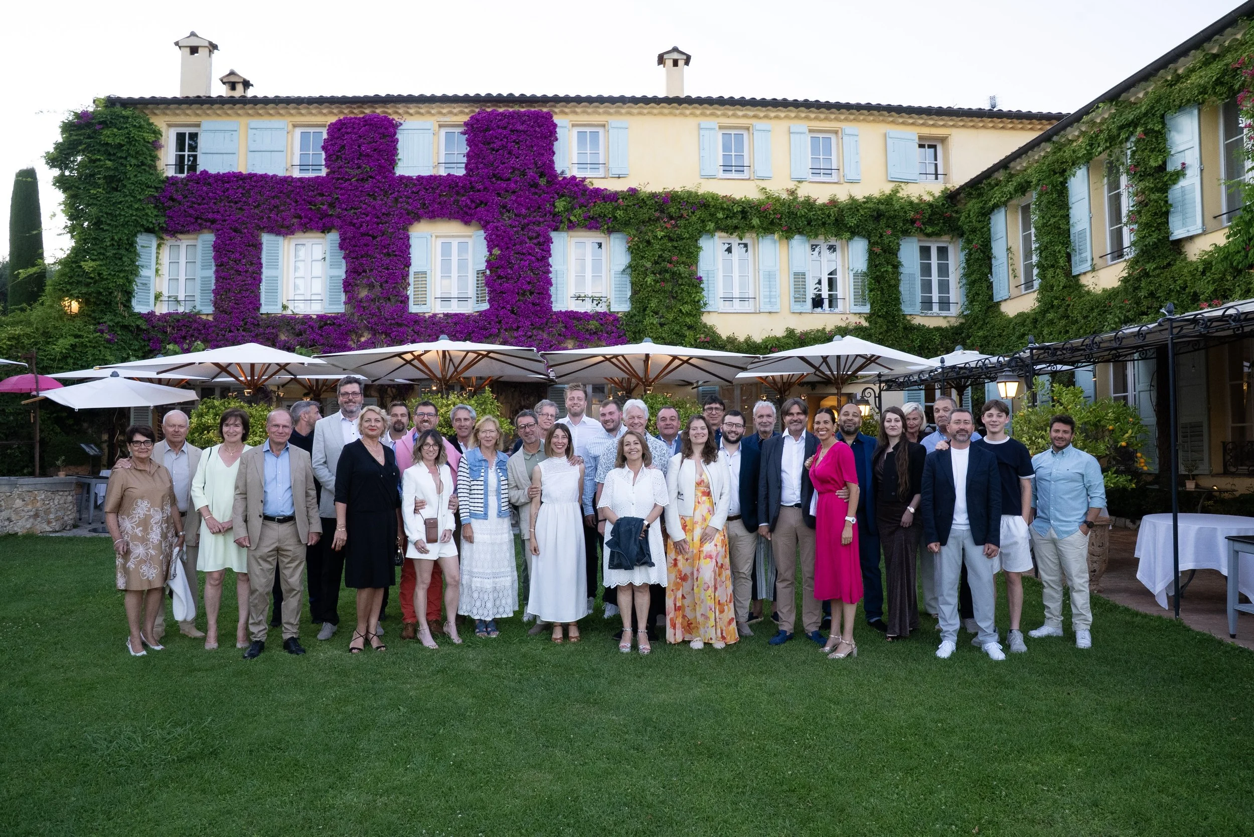 Groupe de personnes posant devant un bâtiment avec des volets bleus et des plantes grimpantes violettes et vertes.