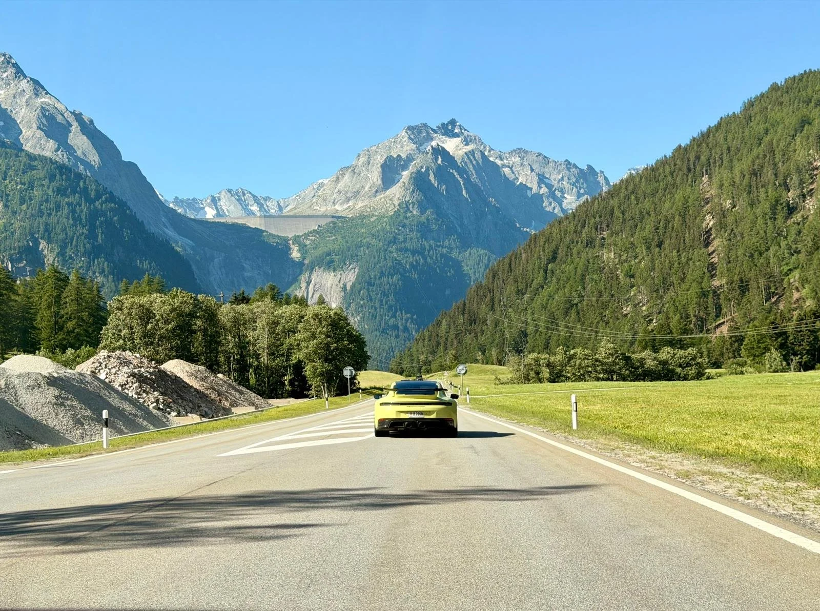 Voiture jaune sur une route traversant un paysage de montagnes avec des forêts et un ciel clair.