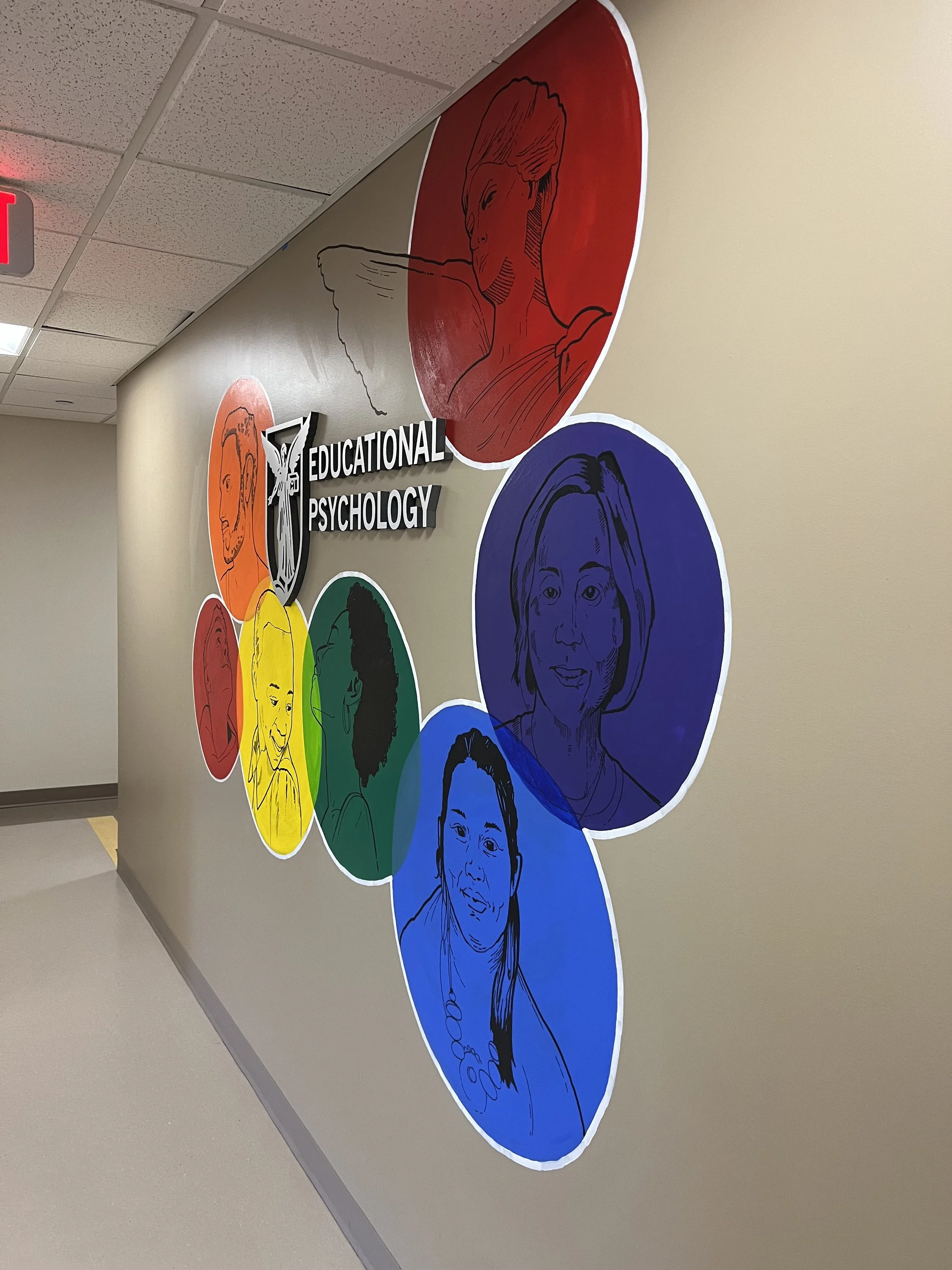 Colorful illustrated portraits of diverse individuals in circles on a wall with a sign reading educational psychology.