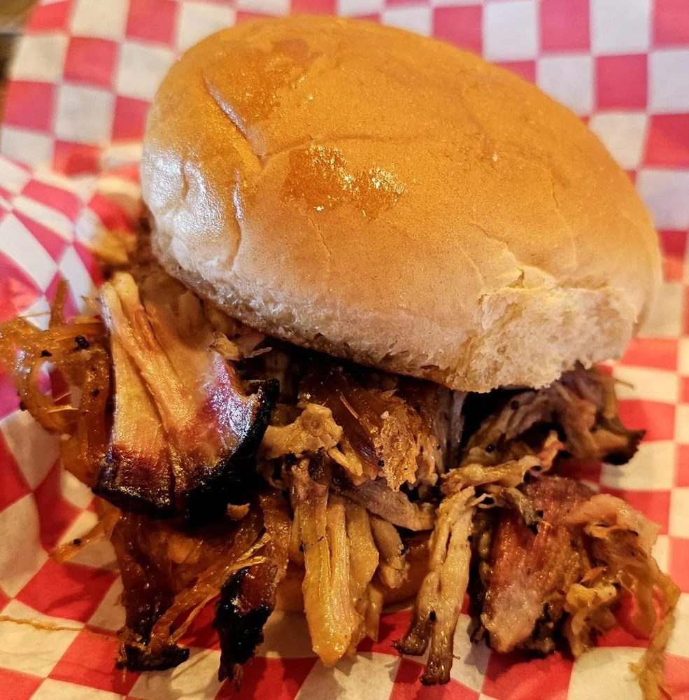 Barbecue pulled pork sandwich on a bun with shredded pork and barbecue sauce on red and white checkered paper.