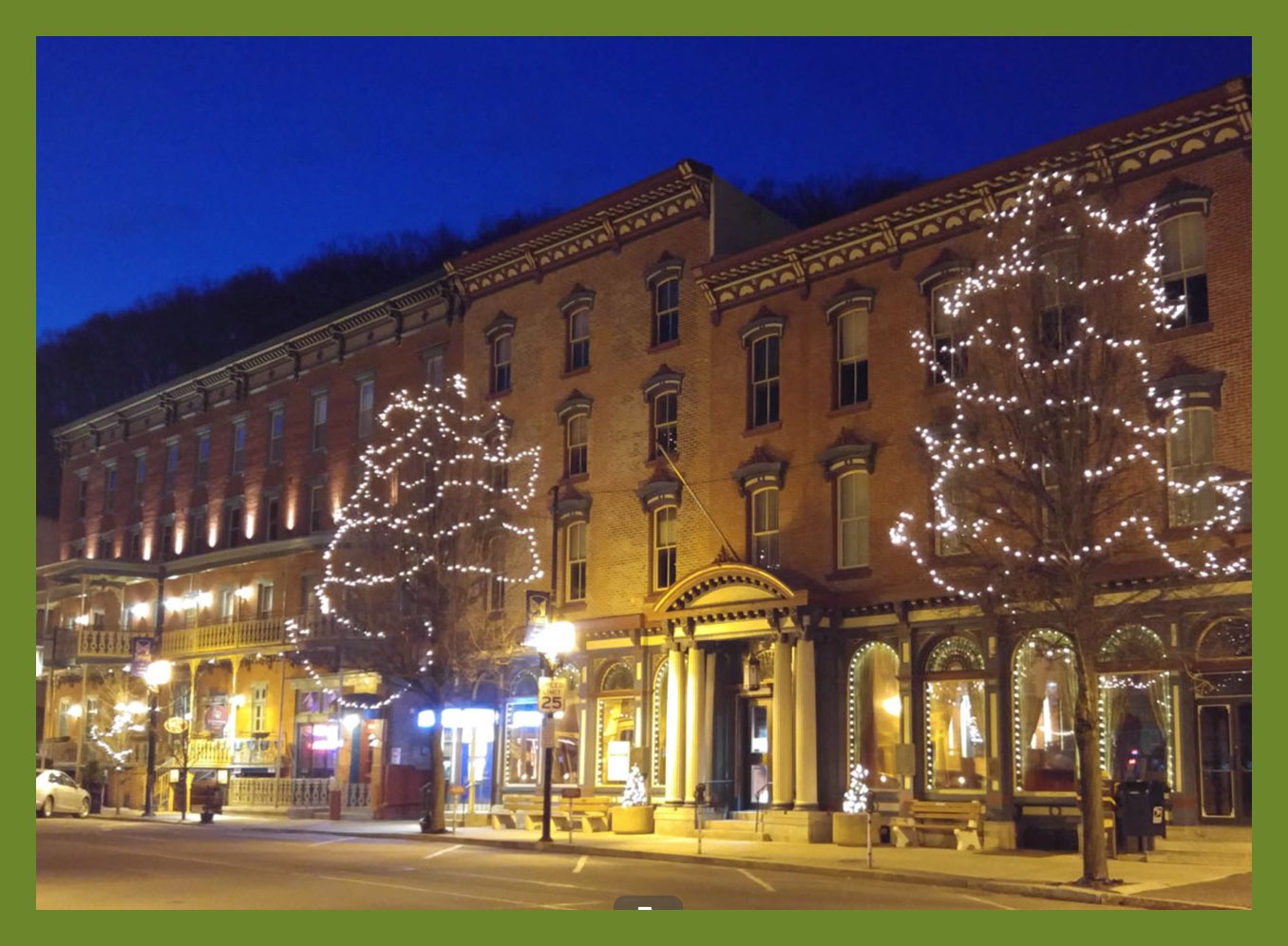 Night view of historic brick buildings decorated with string lights, with trees illuminated in Christmas lights on a street in a small town.