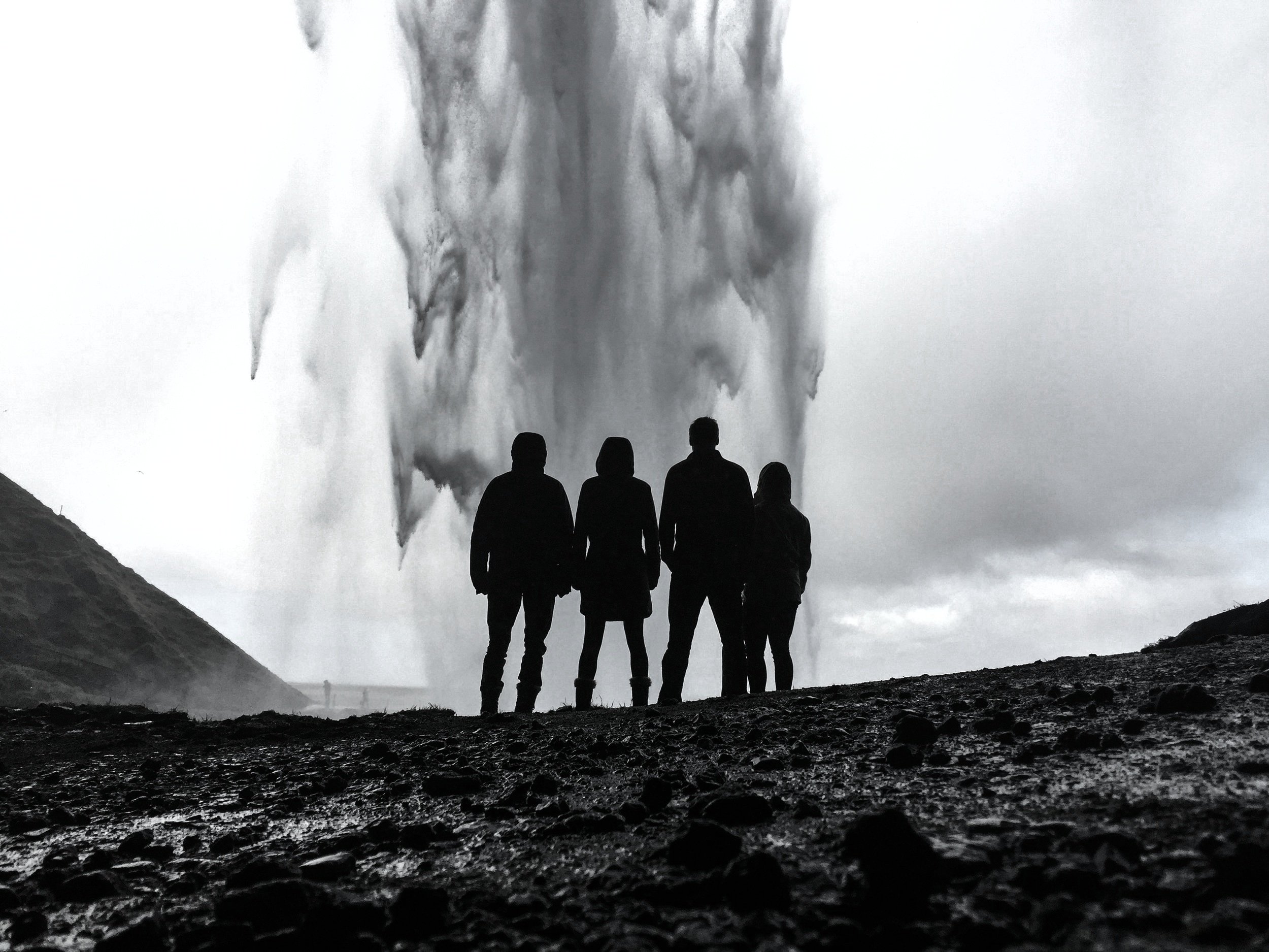 Four people silhouetted from behind, standing in front of a geyser