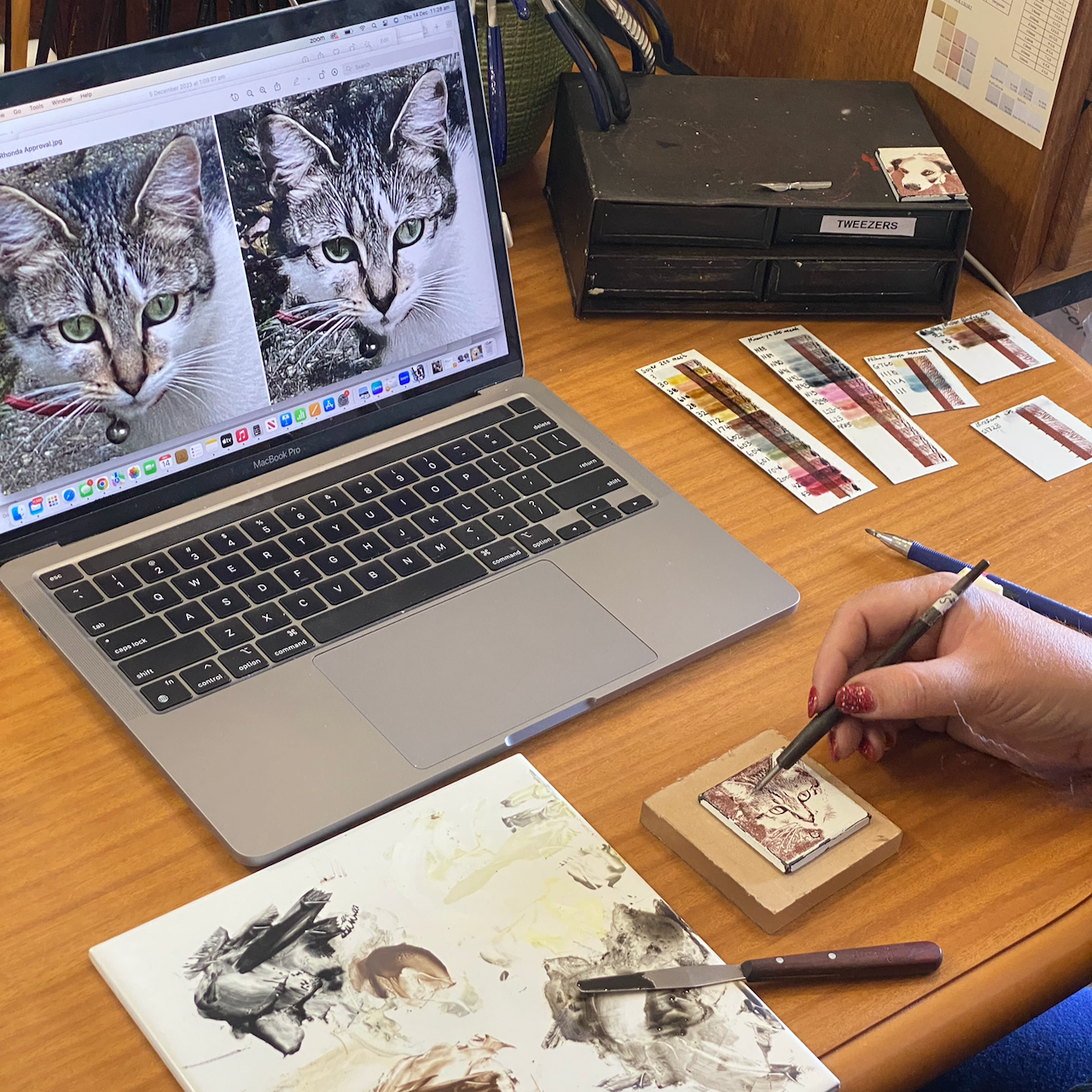 Working on cat enamel art piece with photo reference on computer