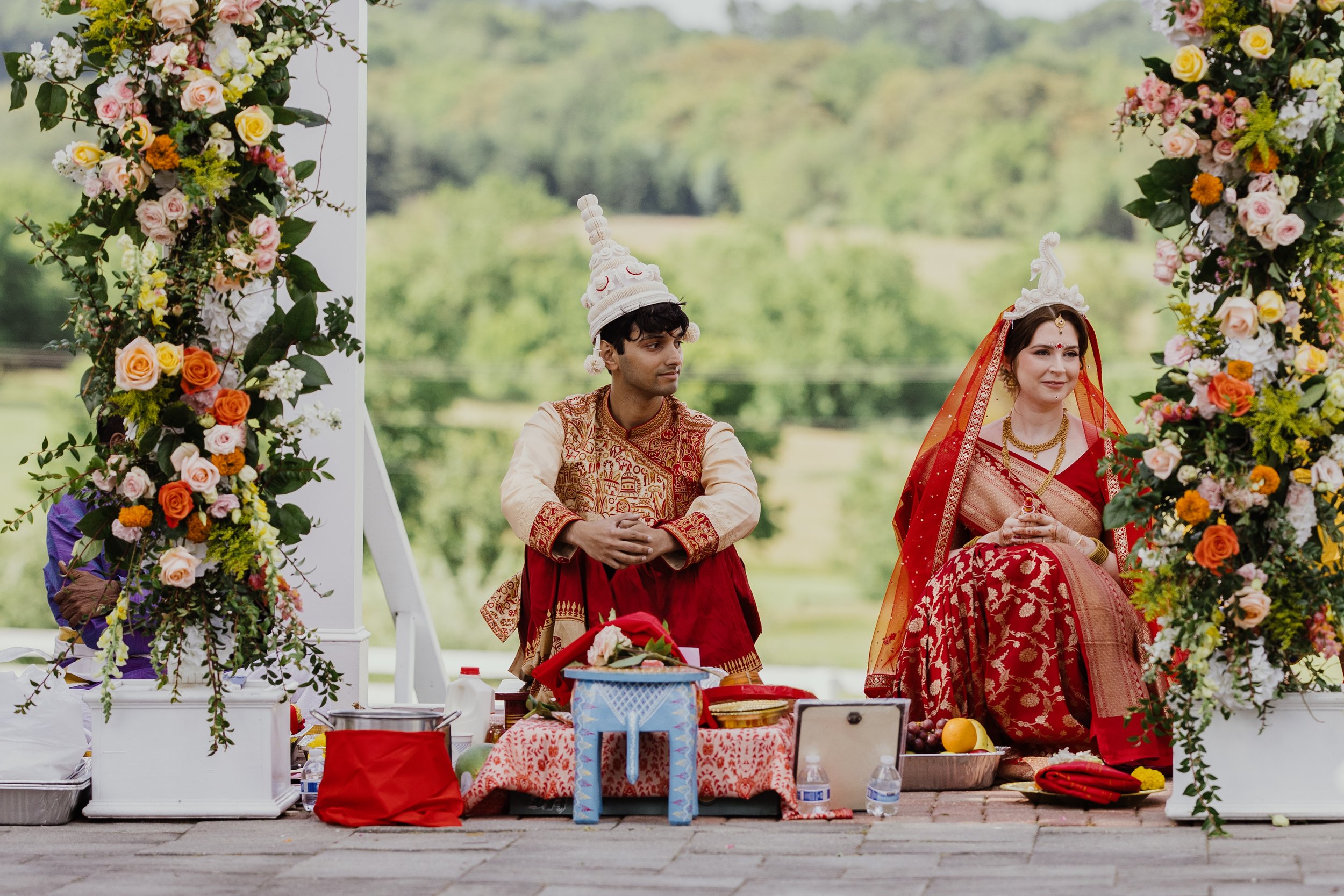 Couple seated beneath a floral ceremony arbor during a South Asian wedding ceremony at Raspberry Plain Manor in Northern Virginia.