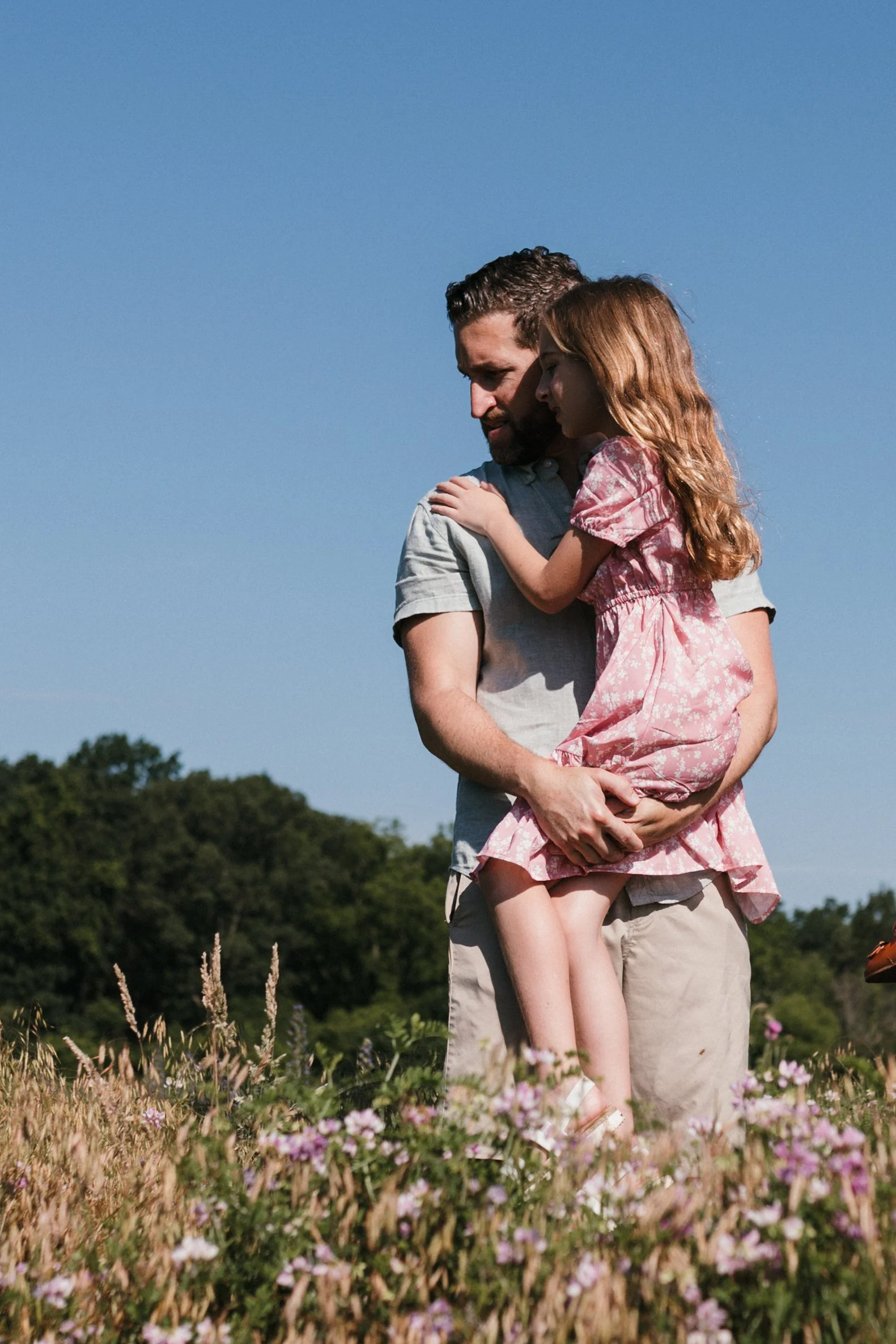 Father holding his daughter during a family photography session at Manassas National Battlefield Park, surrounded by tall grasses and summer light.