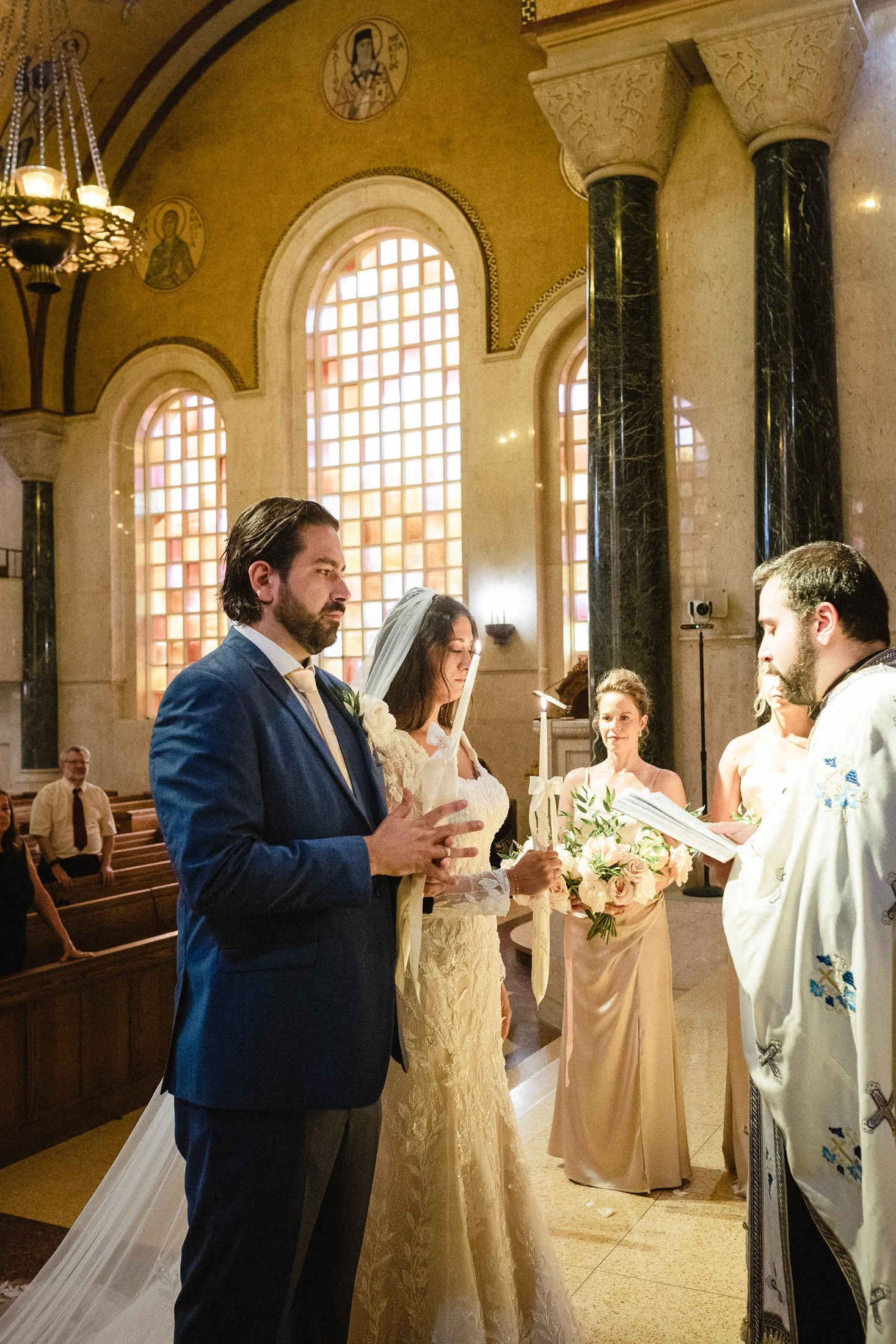 Bride and groom participating in Greek Orthodox wedding ceremony surrounded by candlelight and stained glass at Saint Sophia Greek Orthodox Cathedral