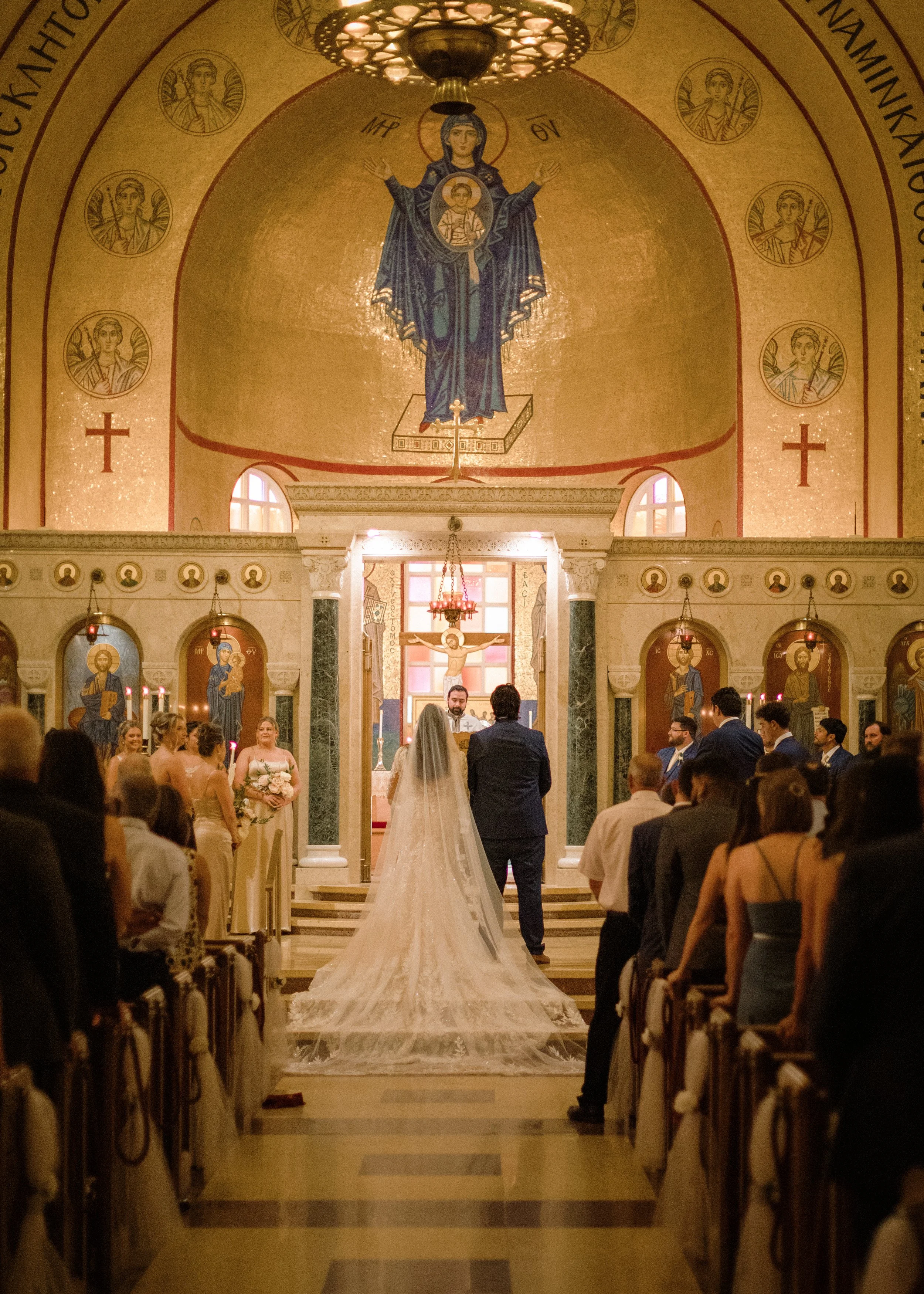 A wedding ceremony taking place inside a church, with the bride and groom standing at the altar surrounded by guests, religious icons, and ornate decor.